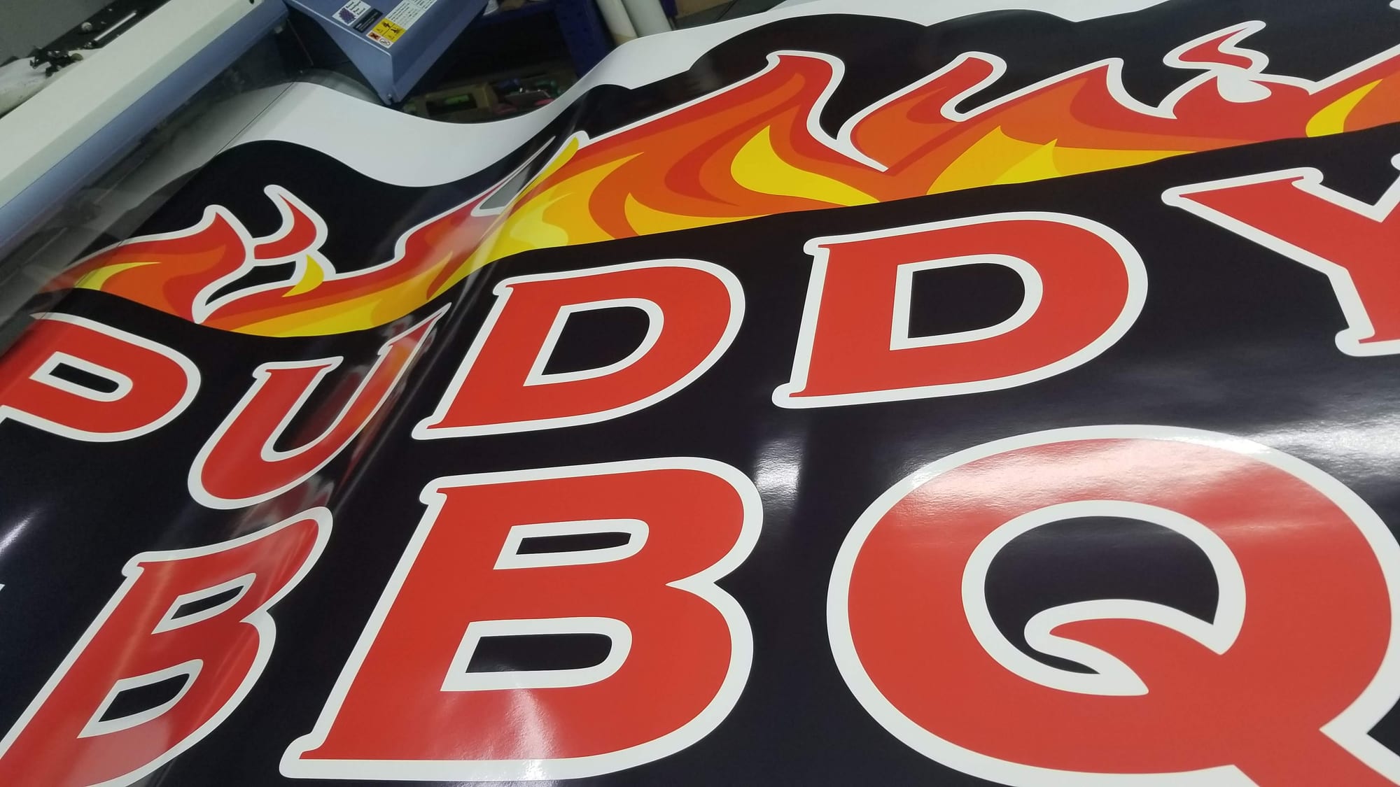 Close-up of a printed BBQ banner with red letters and flame artwork on the printer