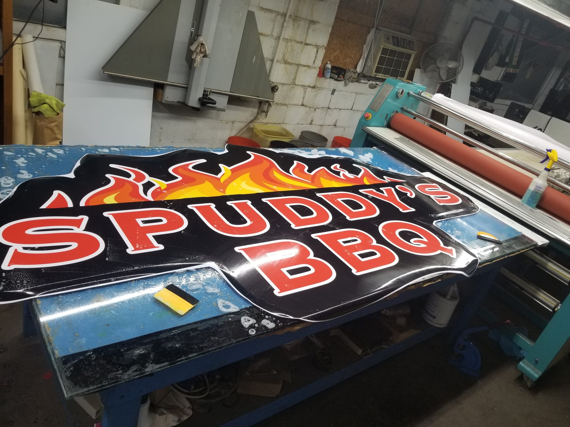 Spuddy's BBQ printed vinyl graphic being applied to a shaped sign face in the shop
