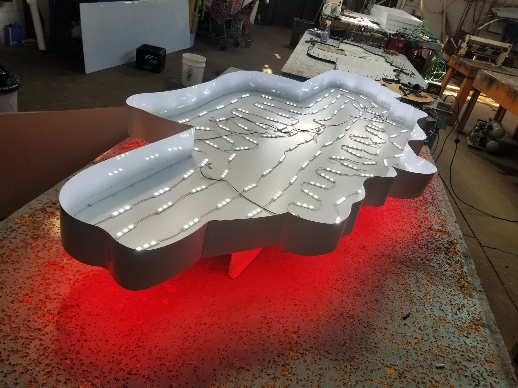 Shaped sign cabinet with LED modules wired and lit inside on a shop table