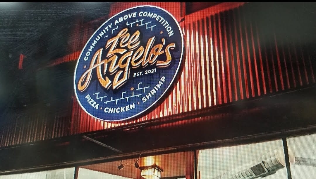 Lit round Zee Angelo's logo cabinet sign mounted above a storefront at night