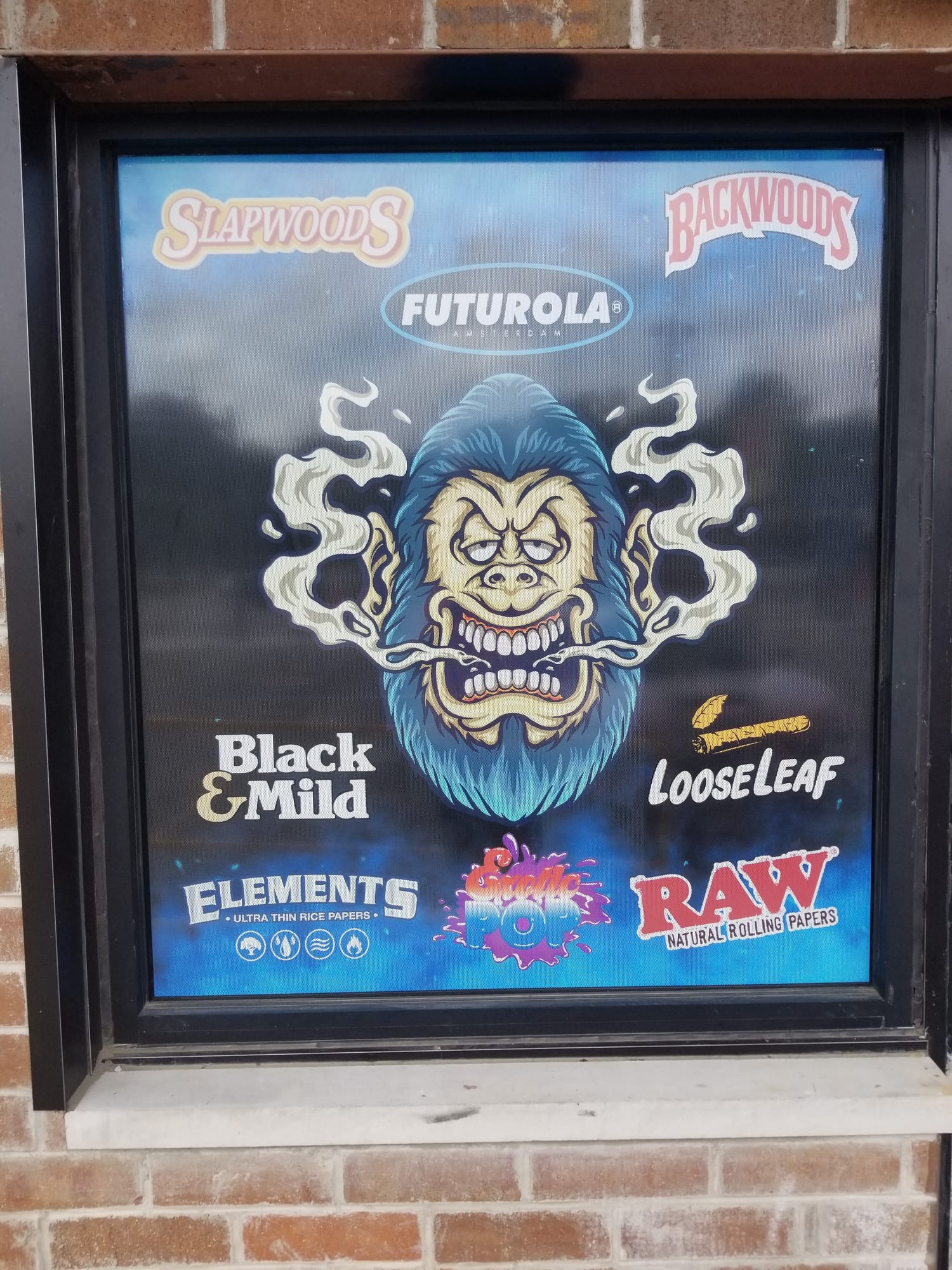 Perforated window graphic with smoke shop product brand logos on a brick storefront