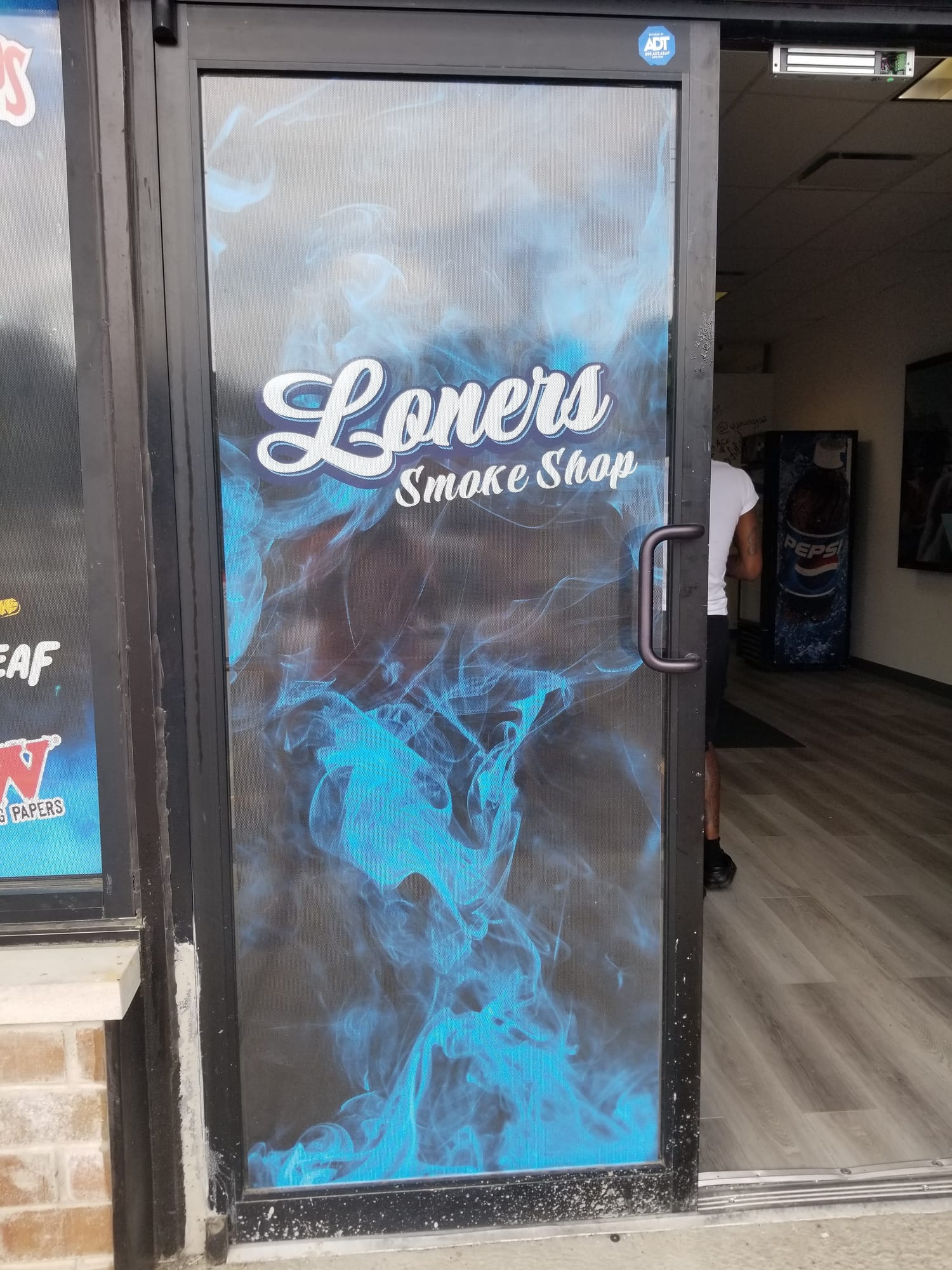 Loners Smoke Shop perforated window graphic covering a glass entry door