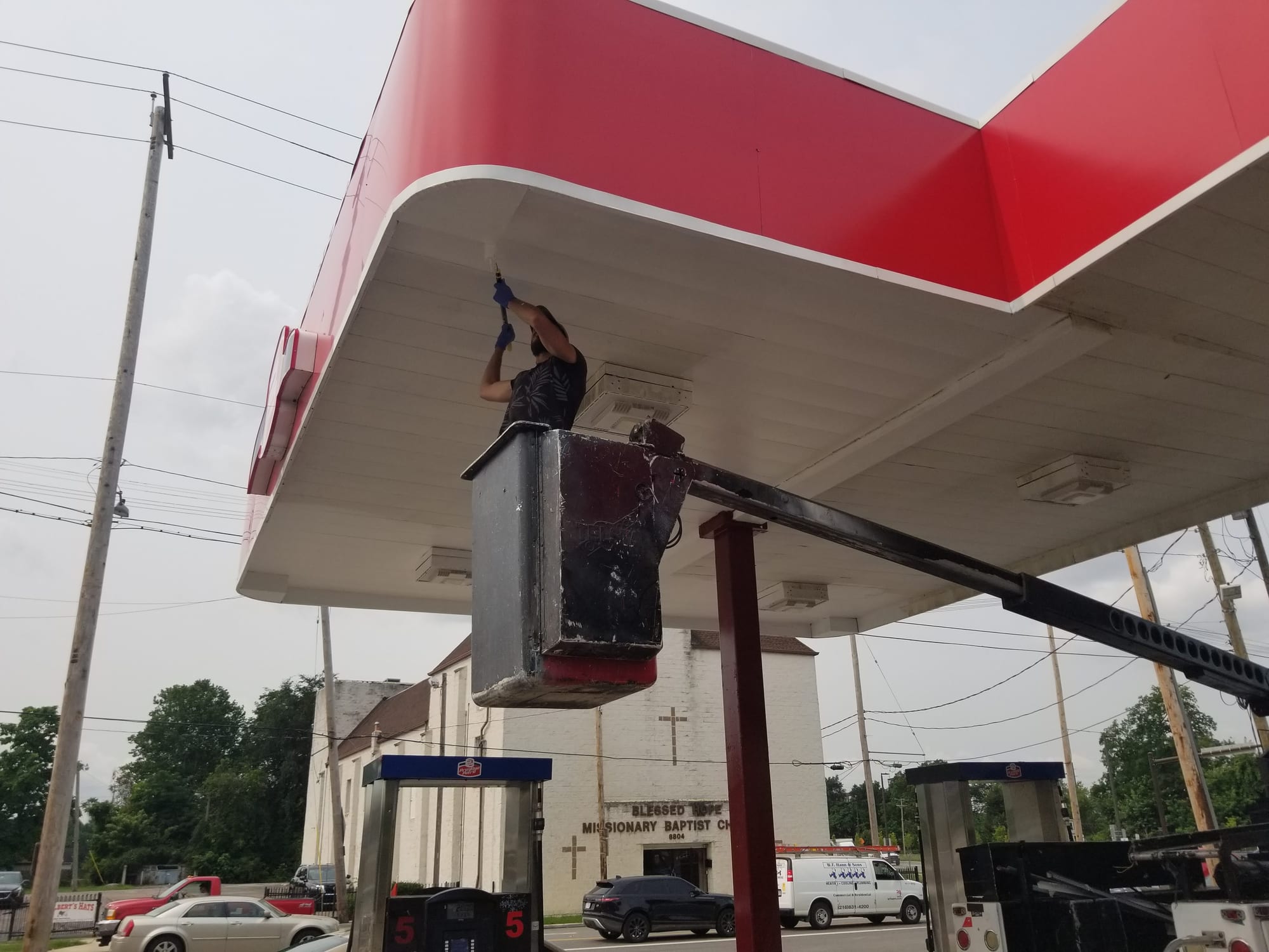 Worker in a bucket lift fastening trim under a red and white gas station canopy fascia