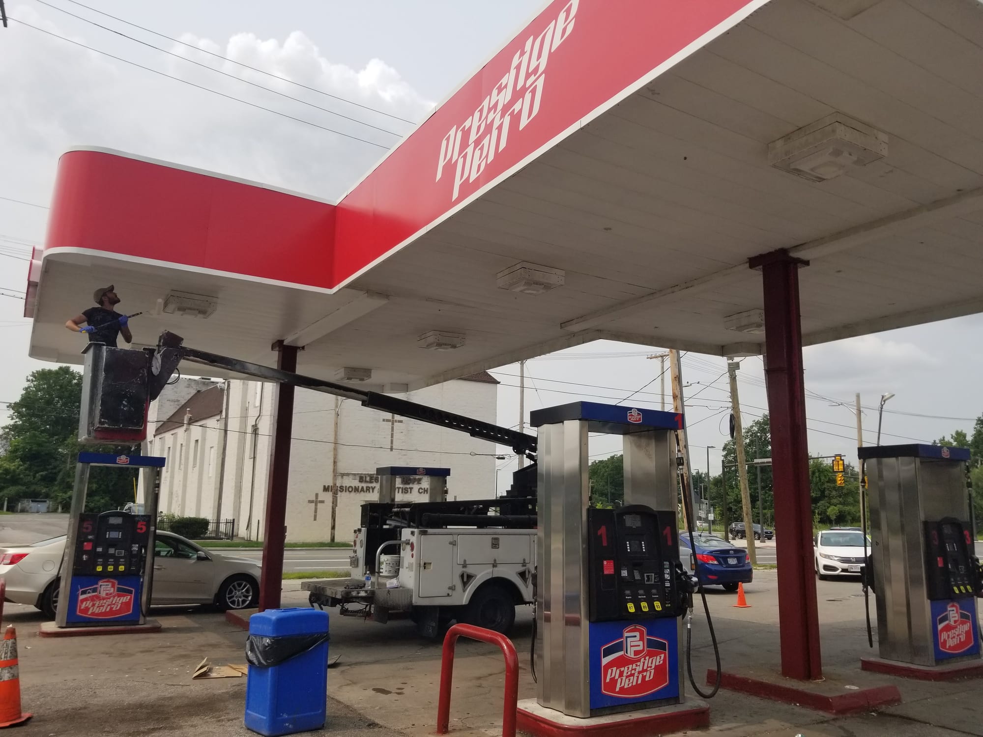 Worker in a bucket lift beside the red Prestige Petro canopy fascia over the pump islands