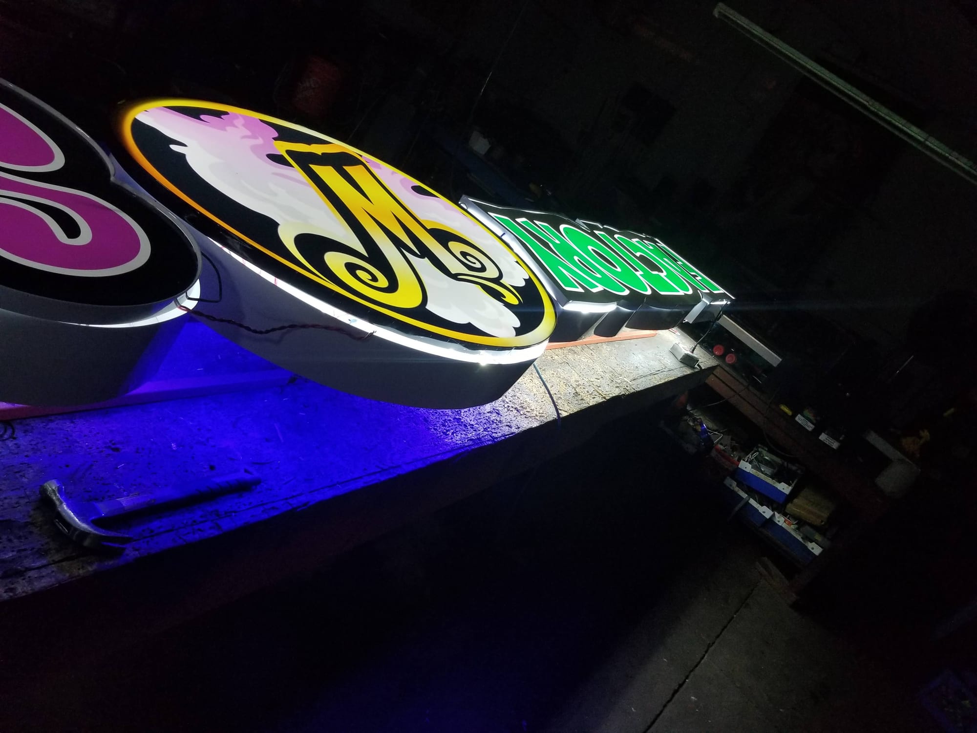 Illuminated oval logo cabinets and lit letters glowing on a dark shop bench