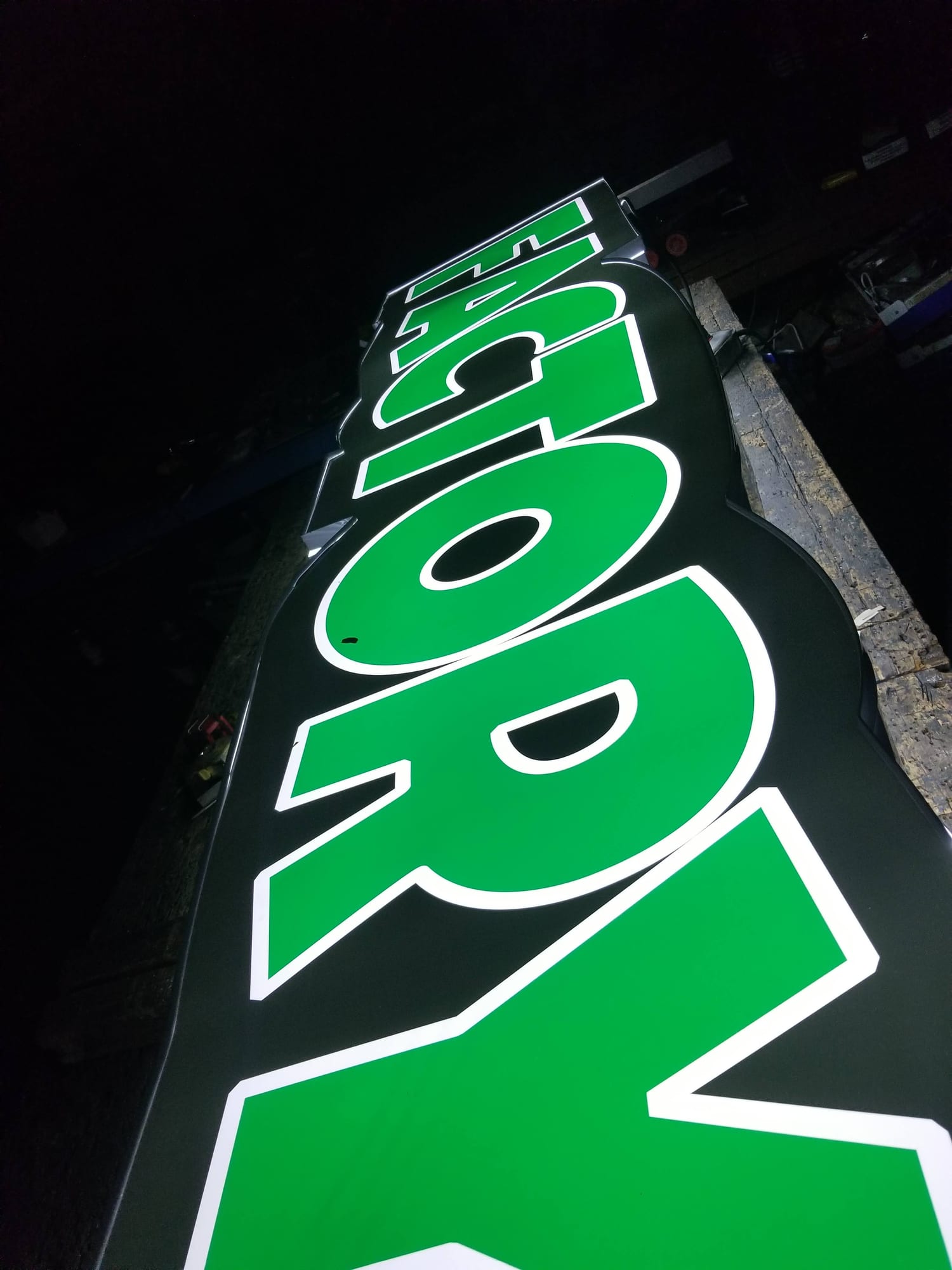 Green face-lit channel letters glowing on a shop bench at night