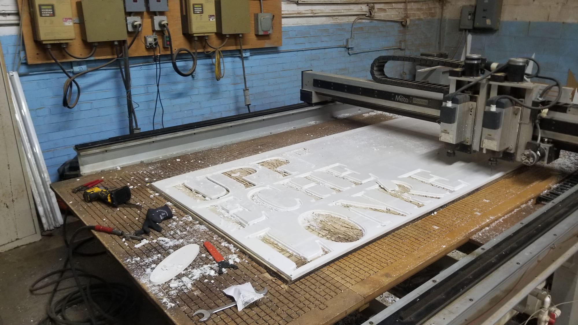 Routed lettering panel on the CNC table with hand tools and gloves alongside