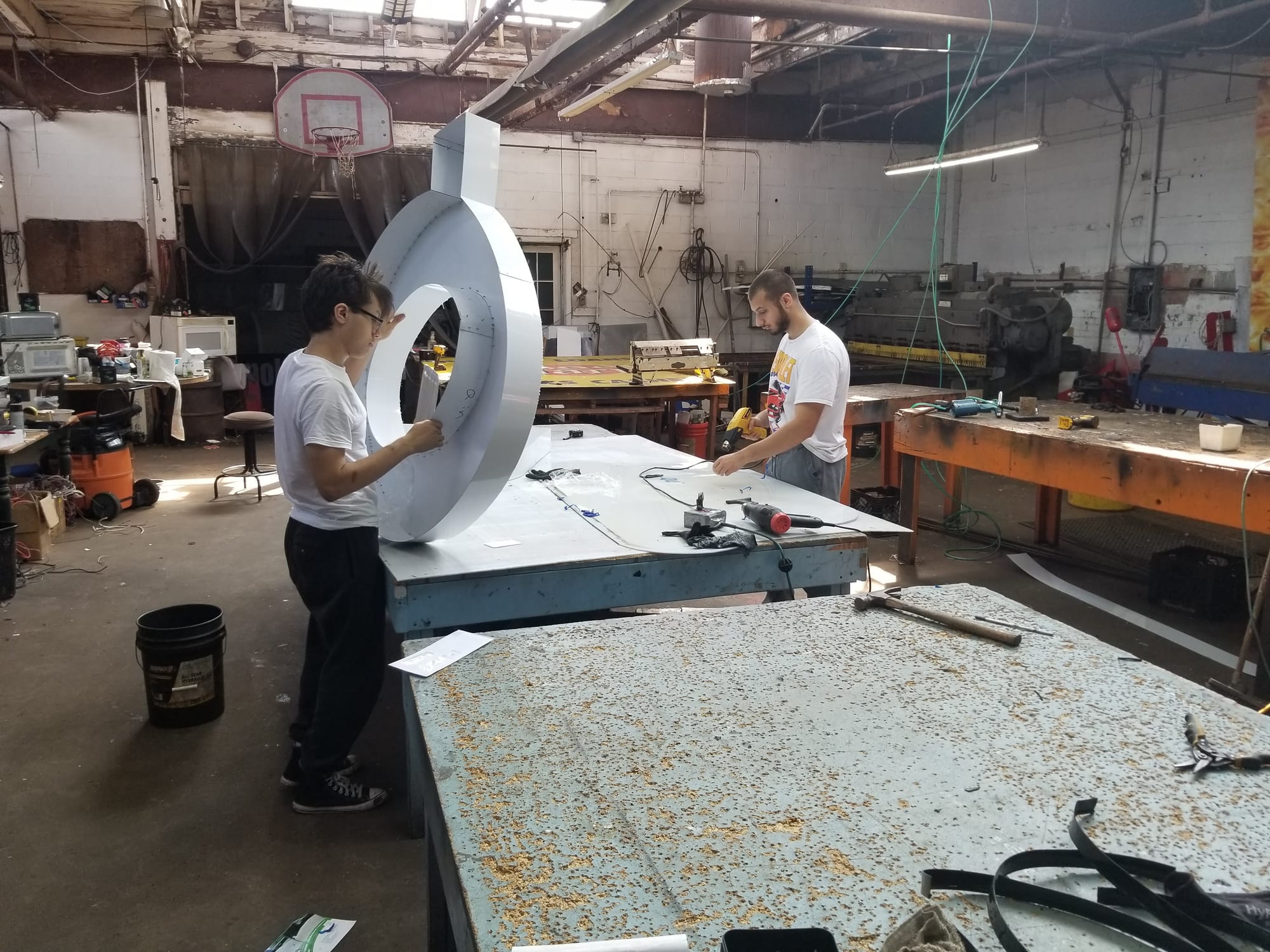 Two workers assembling a large round white channel letter on a shop fabrication table