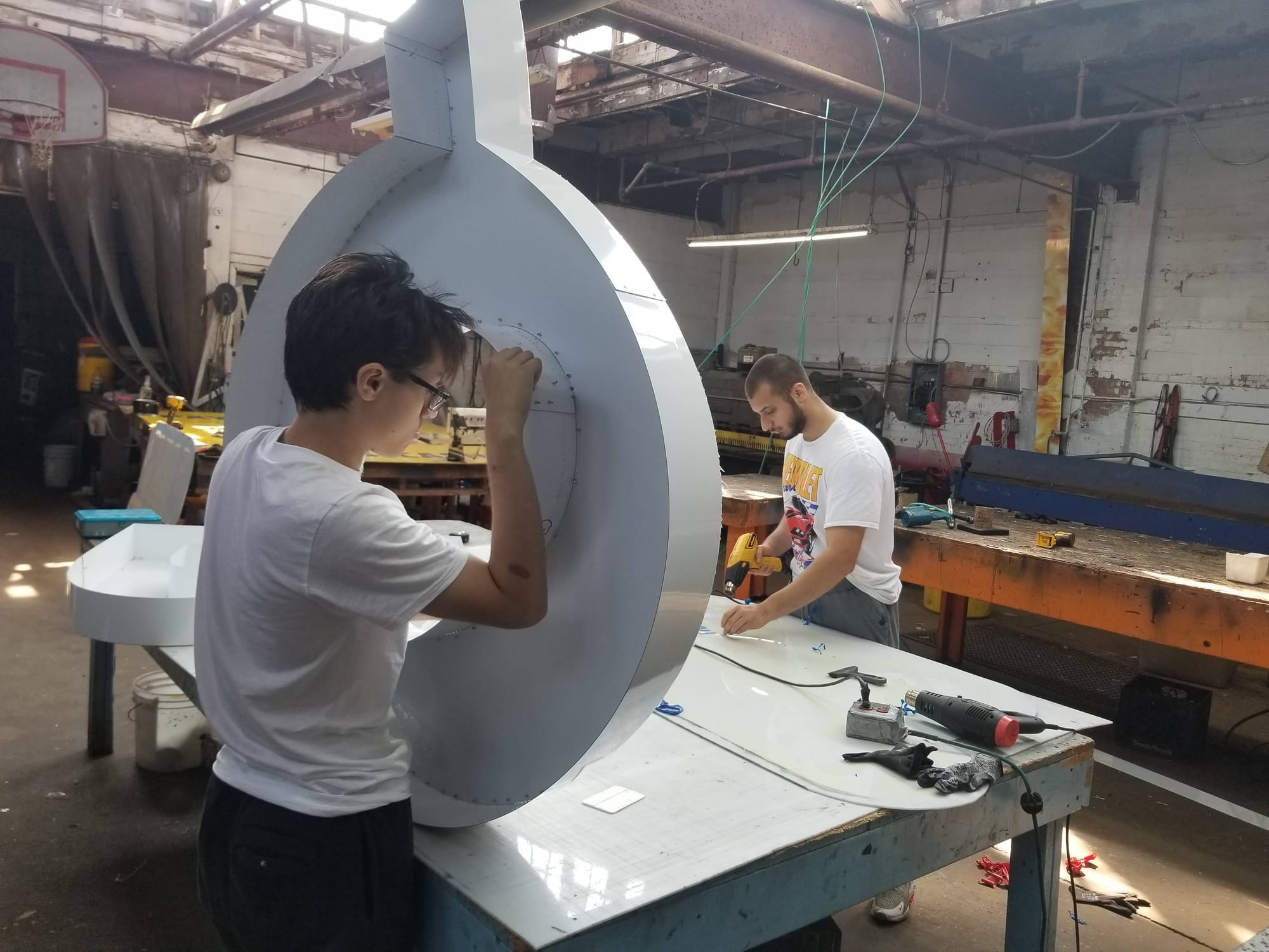 Worker fastening the return on a large round white channel letter in the shop