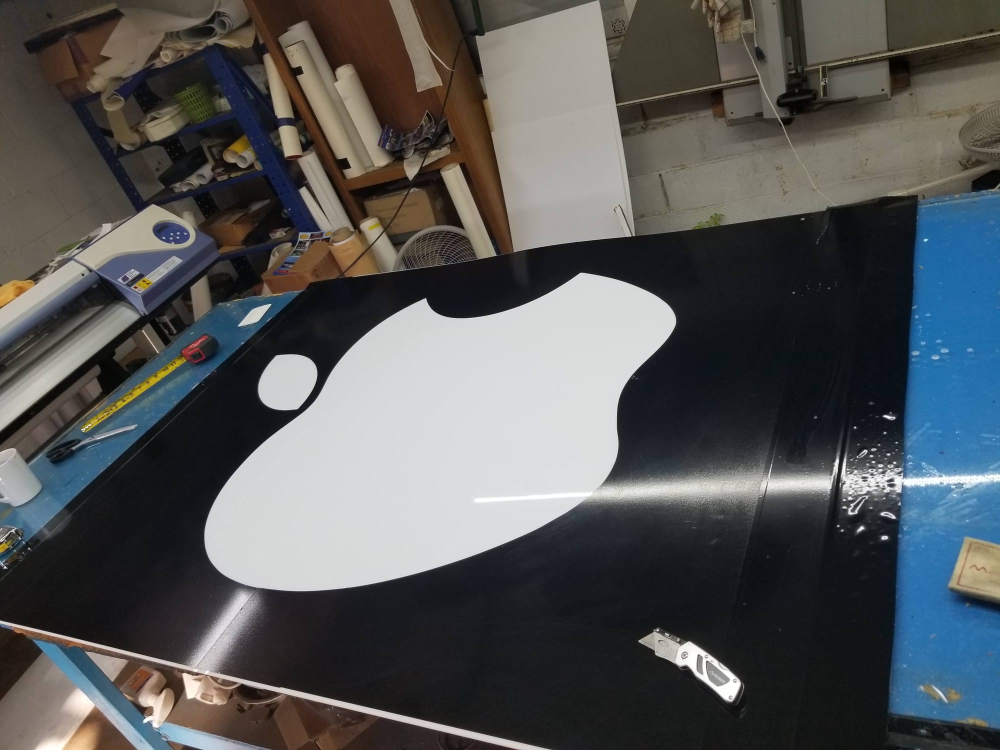 Black panel with a white cut shape applied, on a vinyl shop worktable