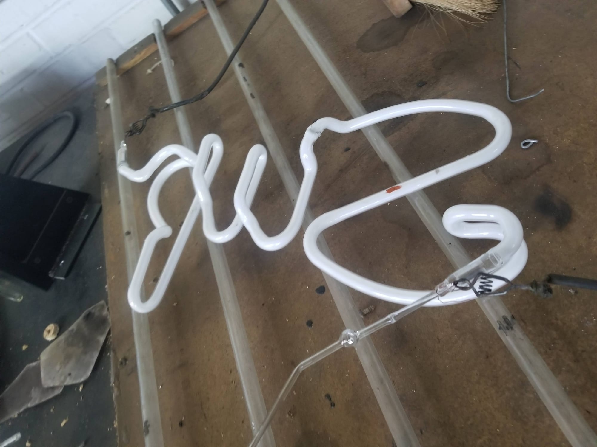 Unlit bent glass neon tube shaped into script lettering on a shop workbench