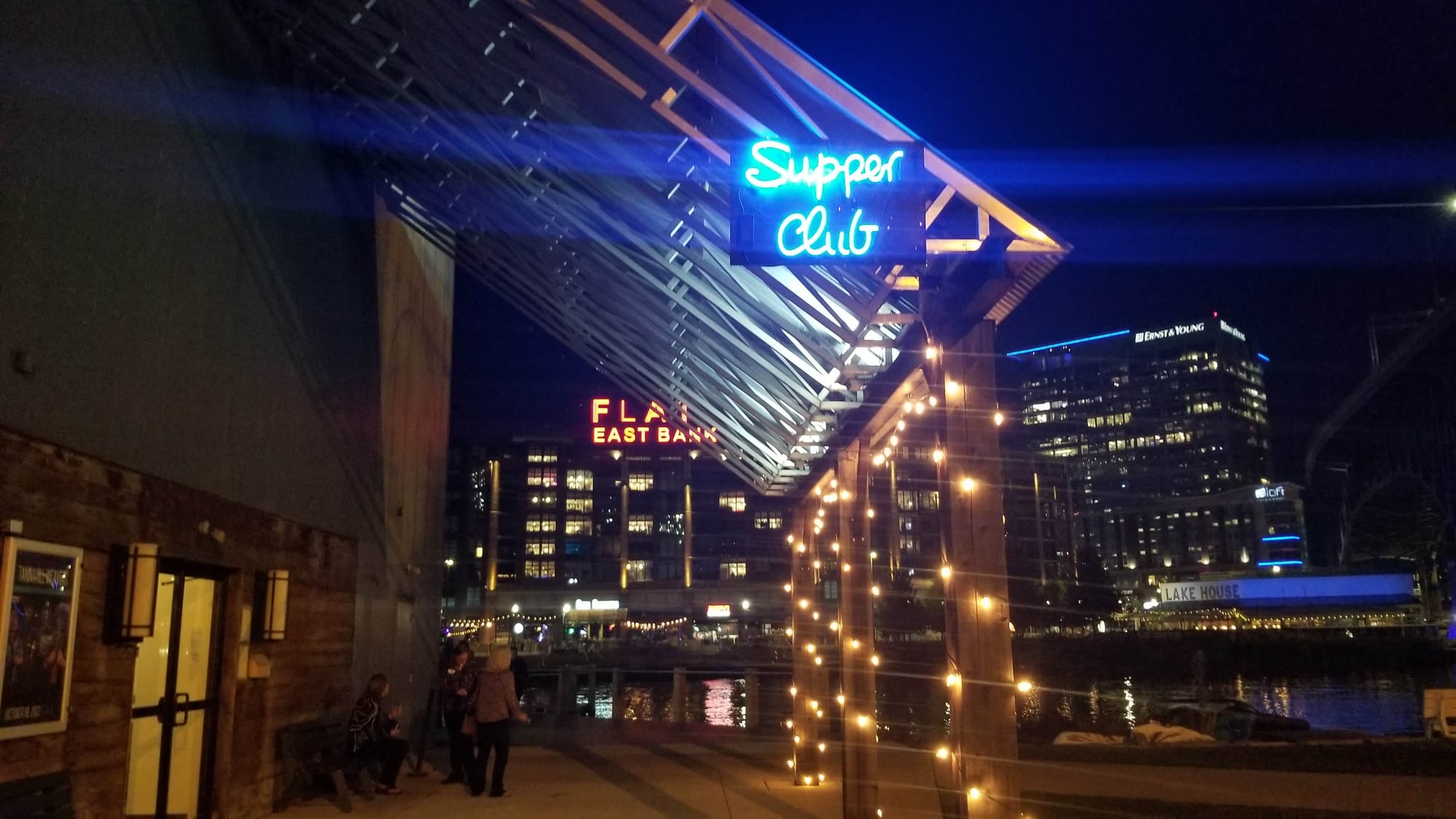 Blue neon Supper Club sign glowing under a timber canopy at night by the river