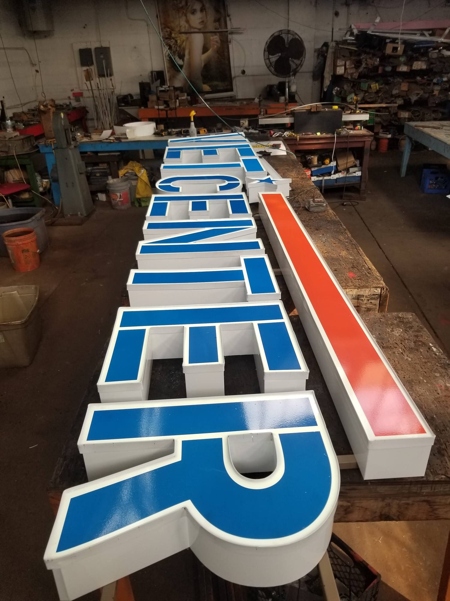 Blue-faced channel letters with white returns and a red accent bar staged on a shop bench