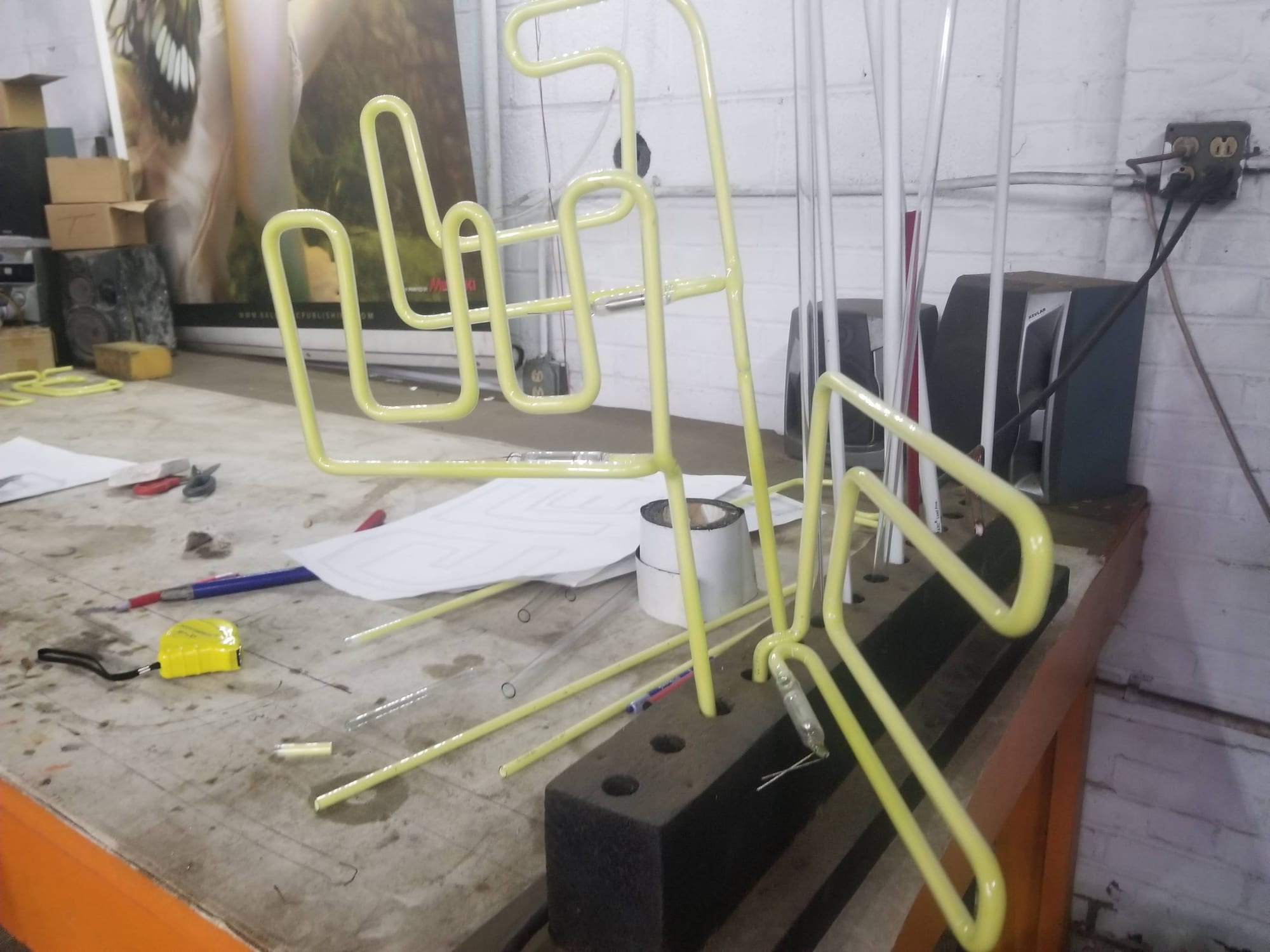 Yellow neon tubing bent into letter shapes standing upright on a neon shop bench