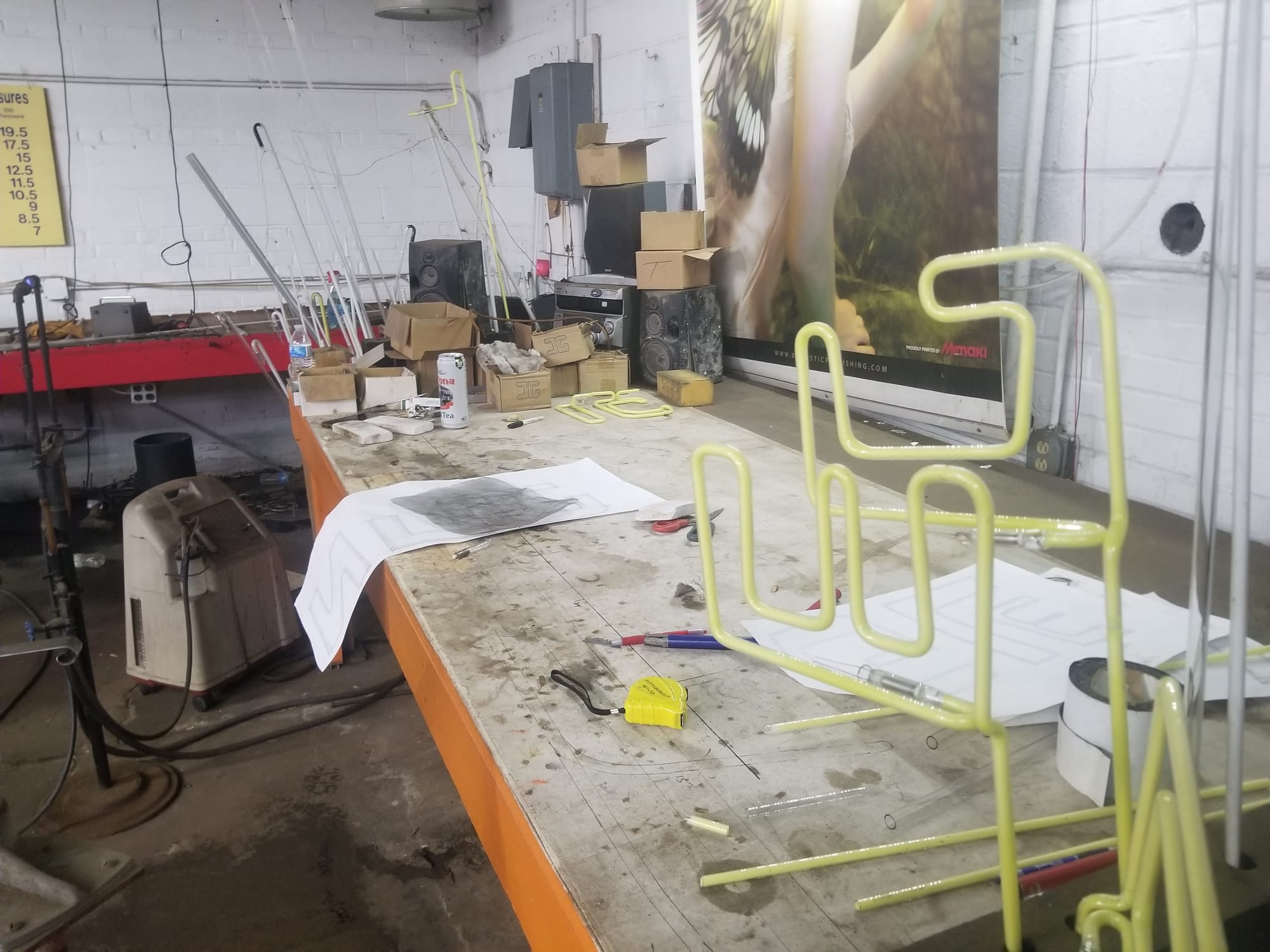Neon shop bench with bent yellow tubing, paper patterns and racks of glass tube stock