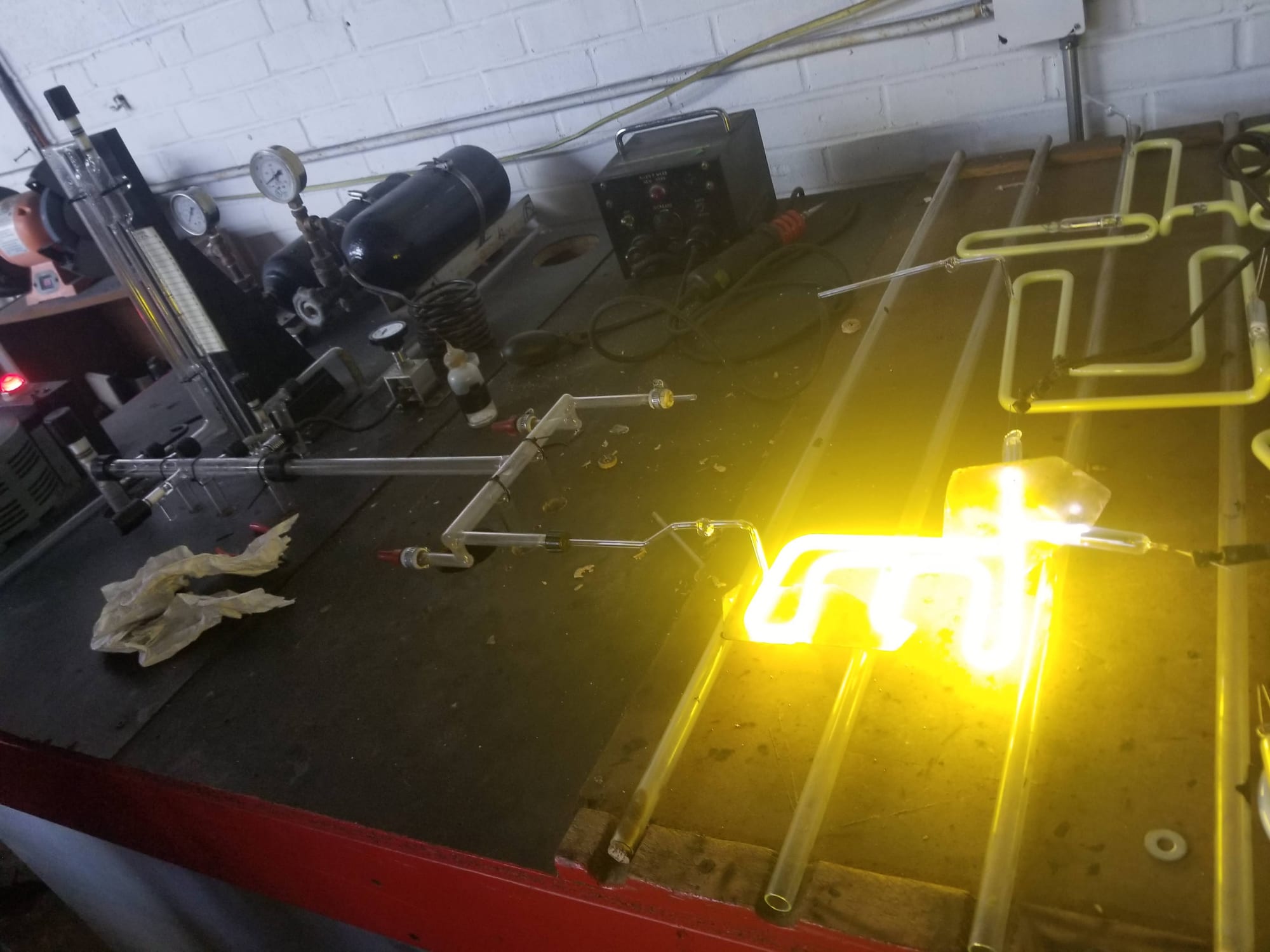 Yellow neon tube glowing on a shop bench beside glass bending and gas fill equipment