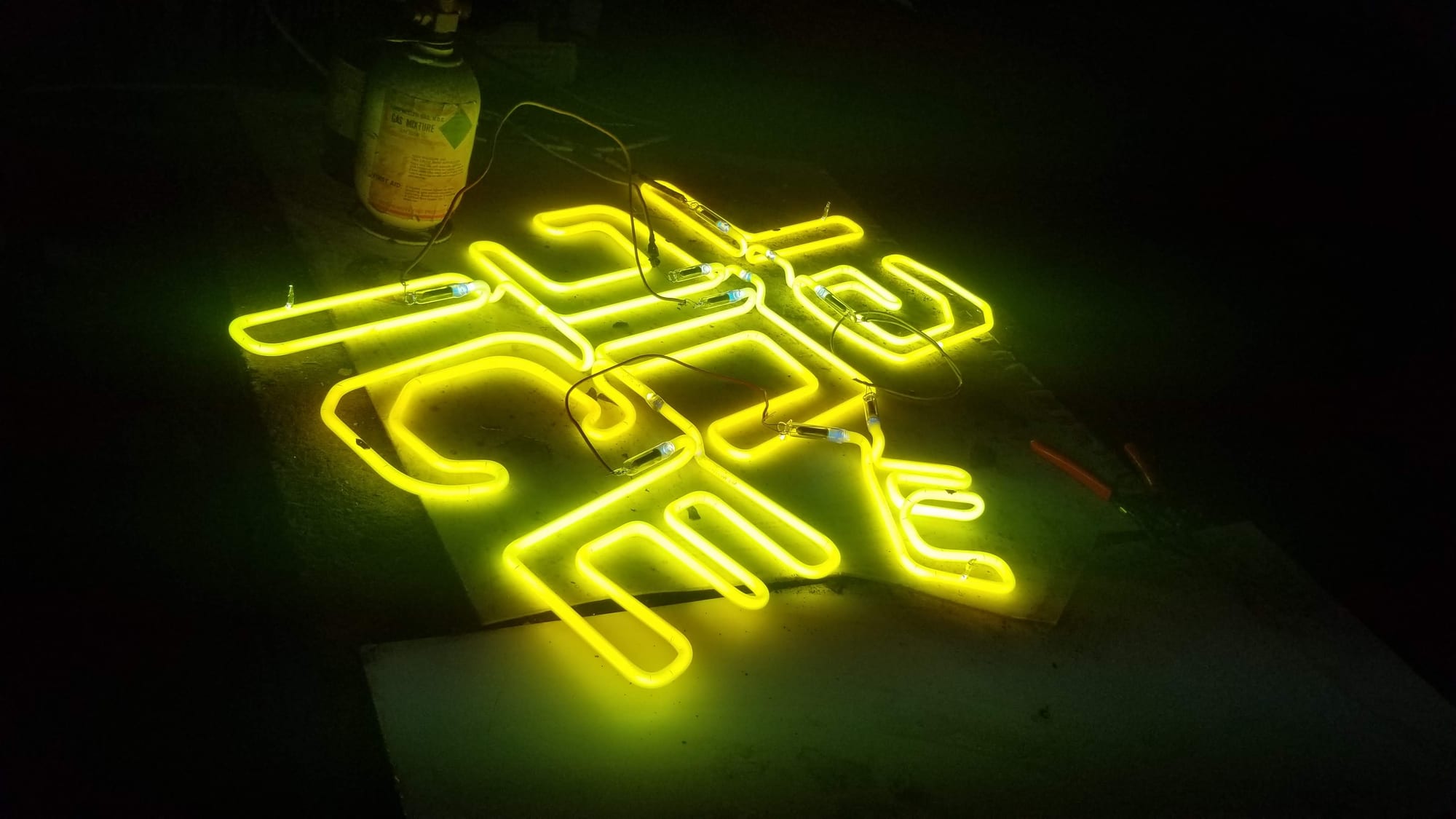 Yellow neon script sign lit up on a dark shop floor during testing