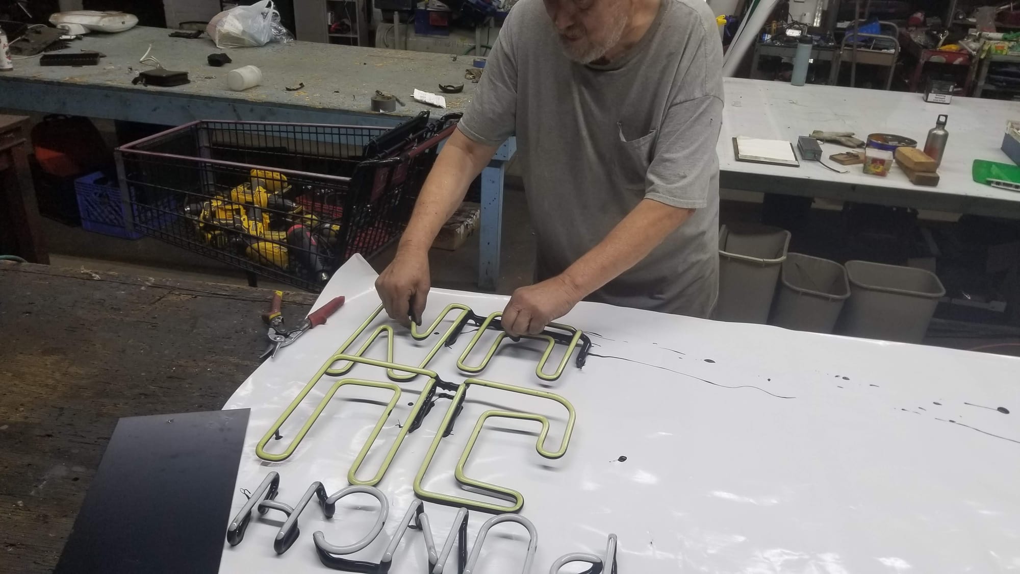Shop worker laying bent neon tubing into black channel letters on a workbench