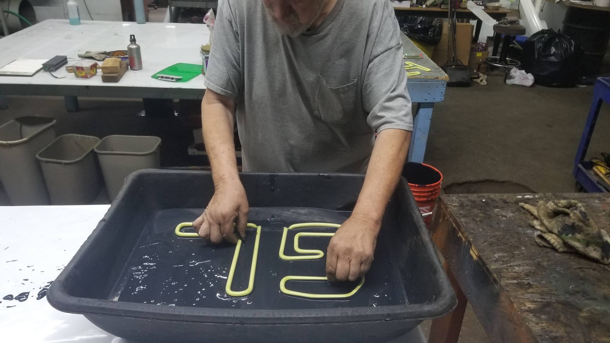 Shop worker rinsing bent yellow neon tubing in a wash tray