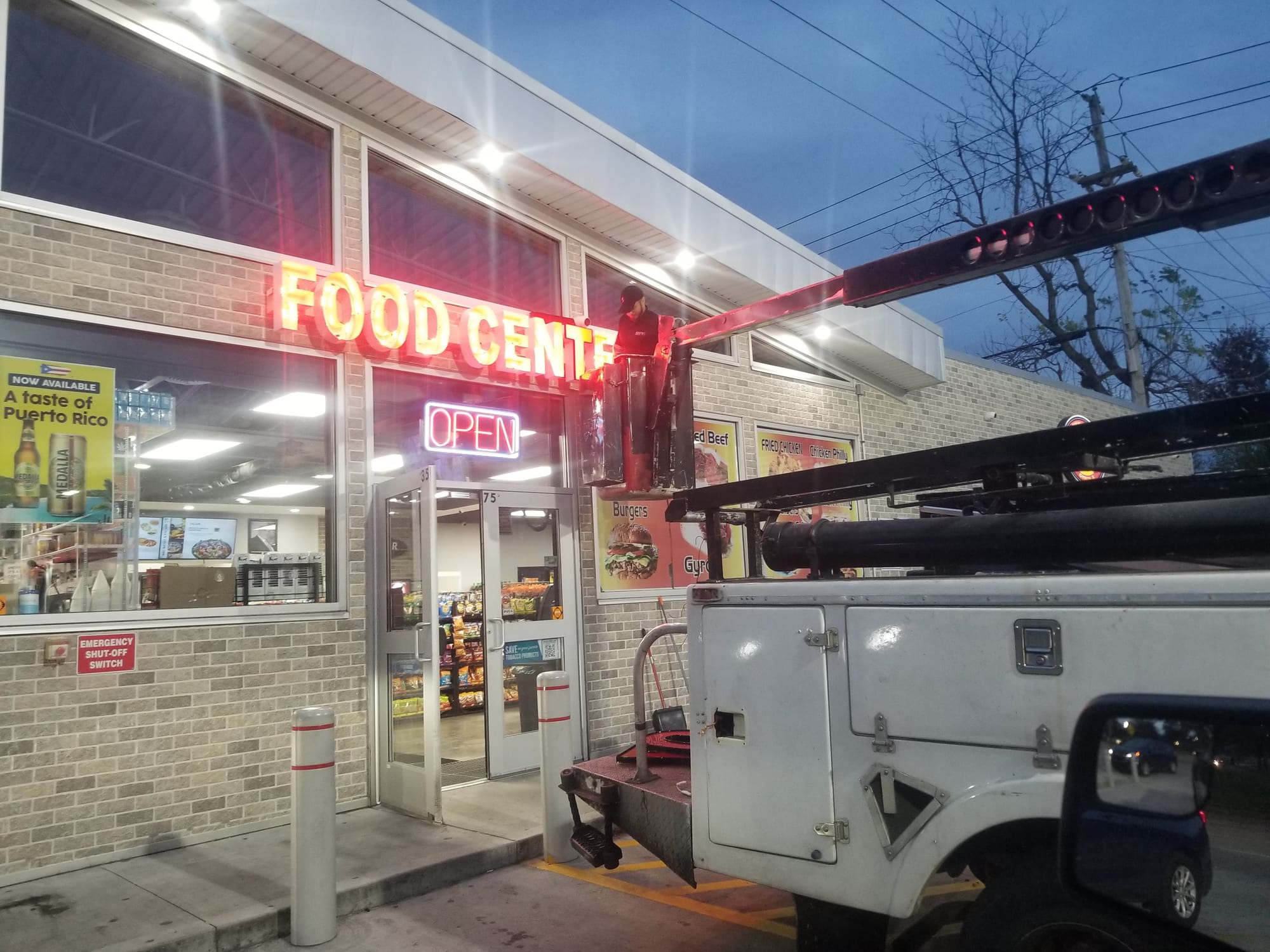 Bucket truck crew servicing lit FOOD CENTER letters above a store entrance at dusk