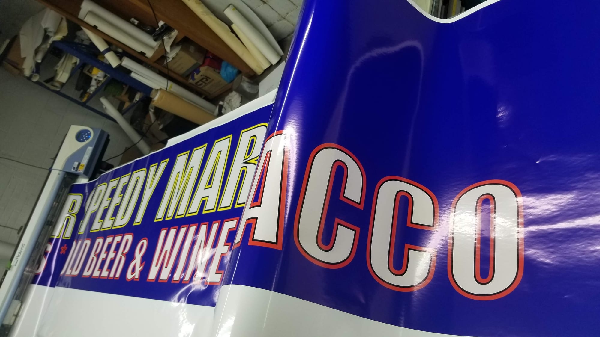 Printed Speedy Mart vinyl banner coming off a Roland wide format printer