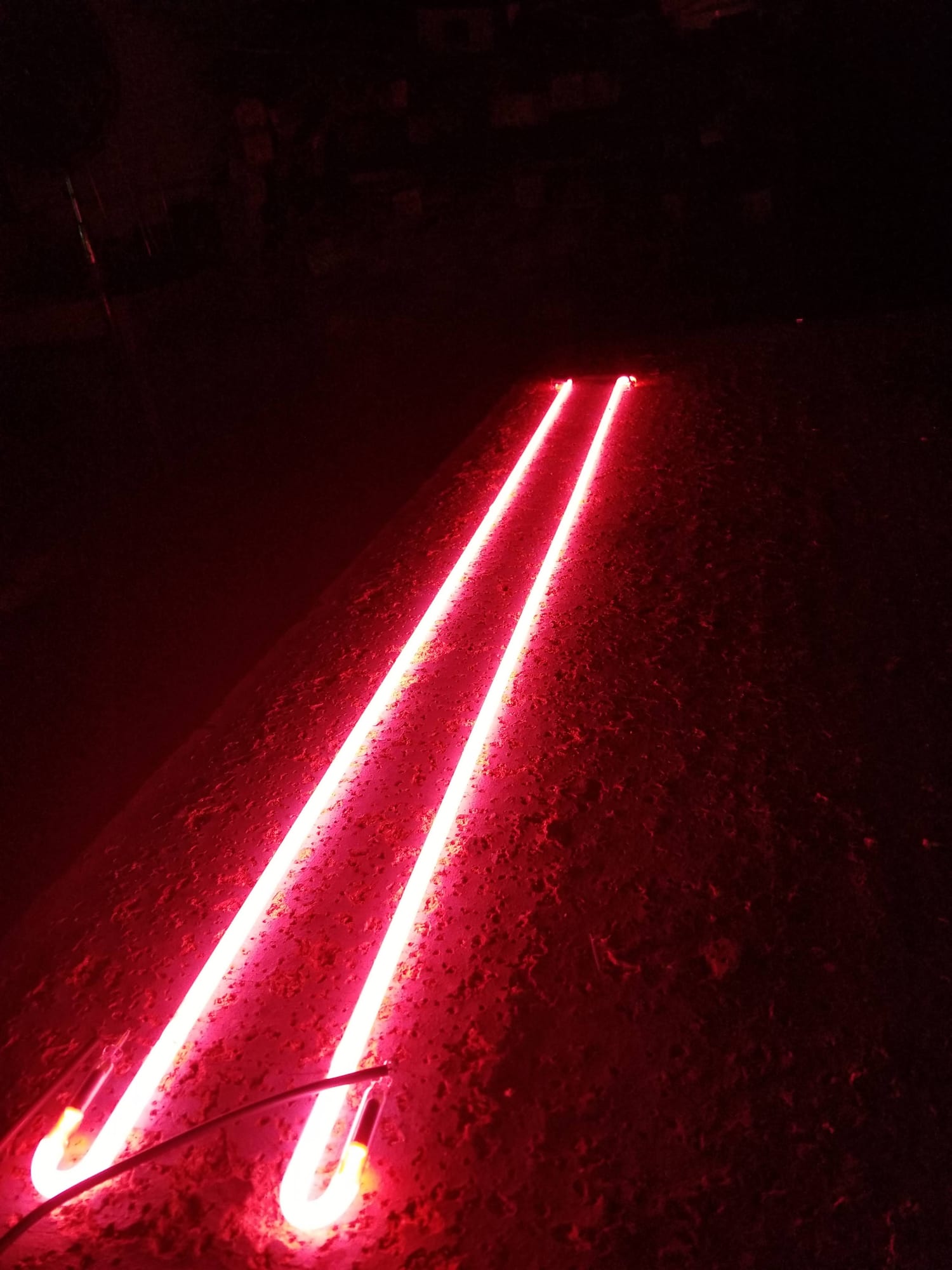 Two long red neon tubes lit on a dark shop floor
