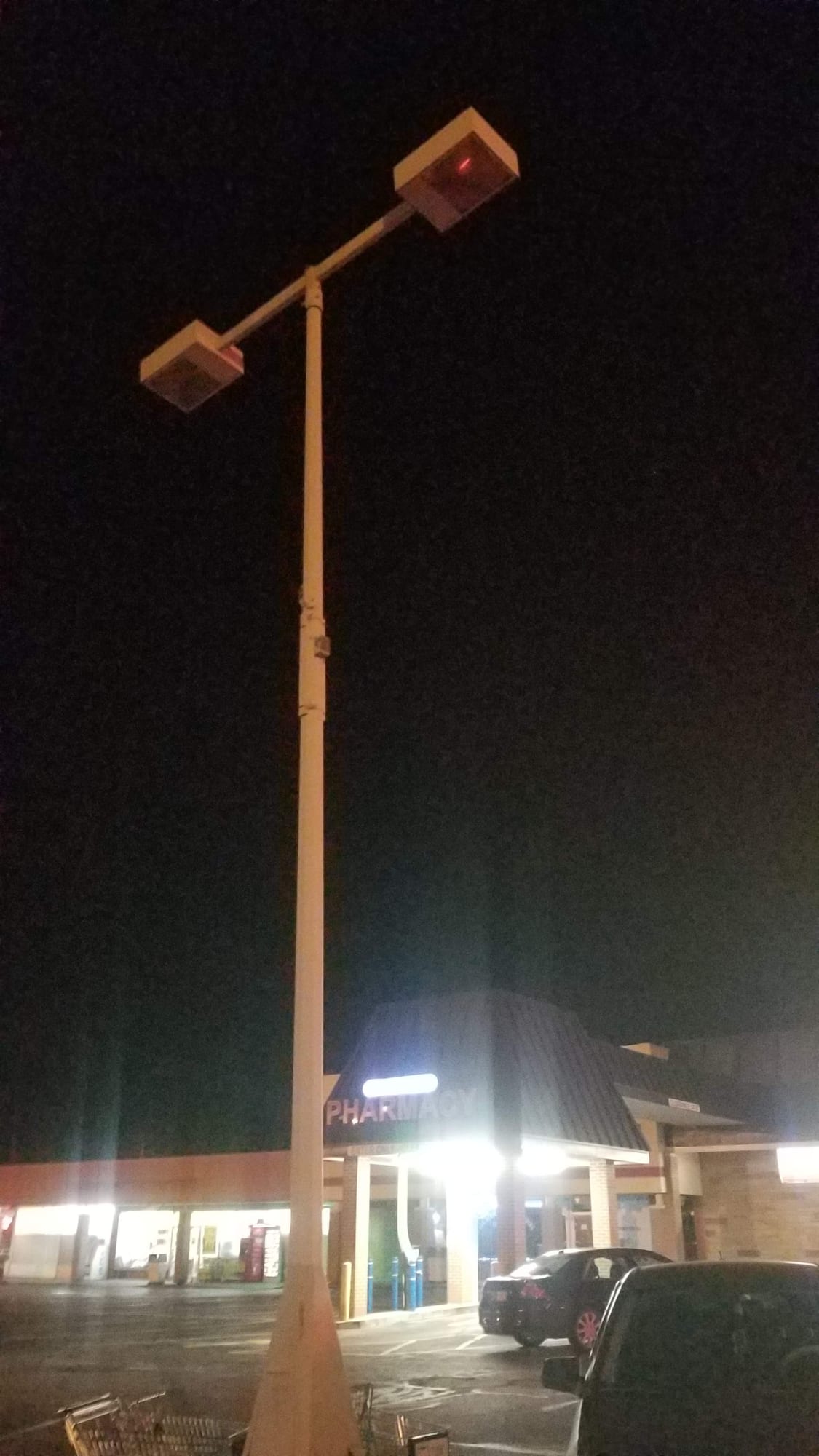 Parking lot light pole at night outside a pharmacy storefront