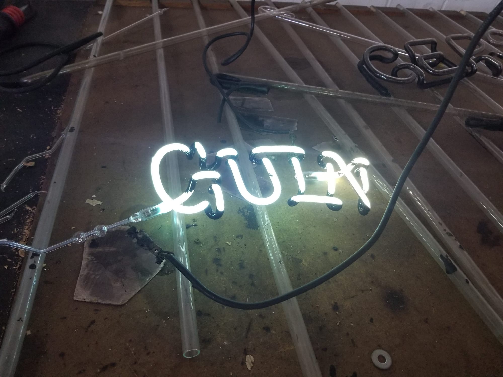 White neon script lit on a glass bending table among clear tubing