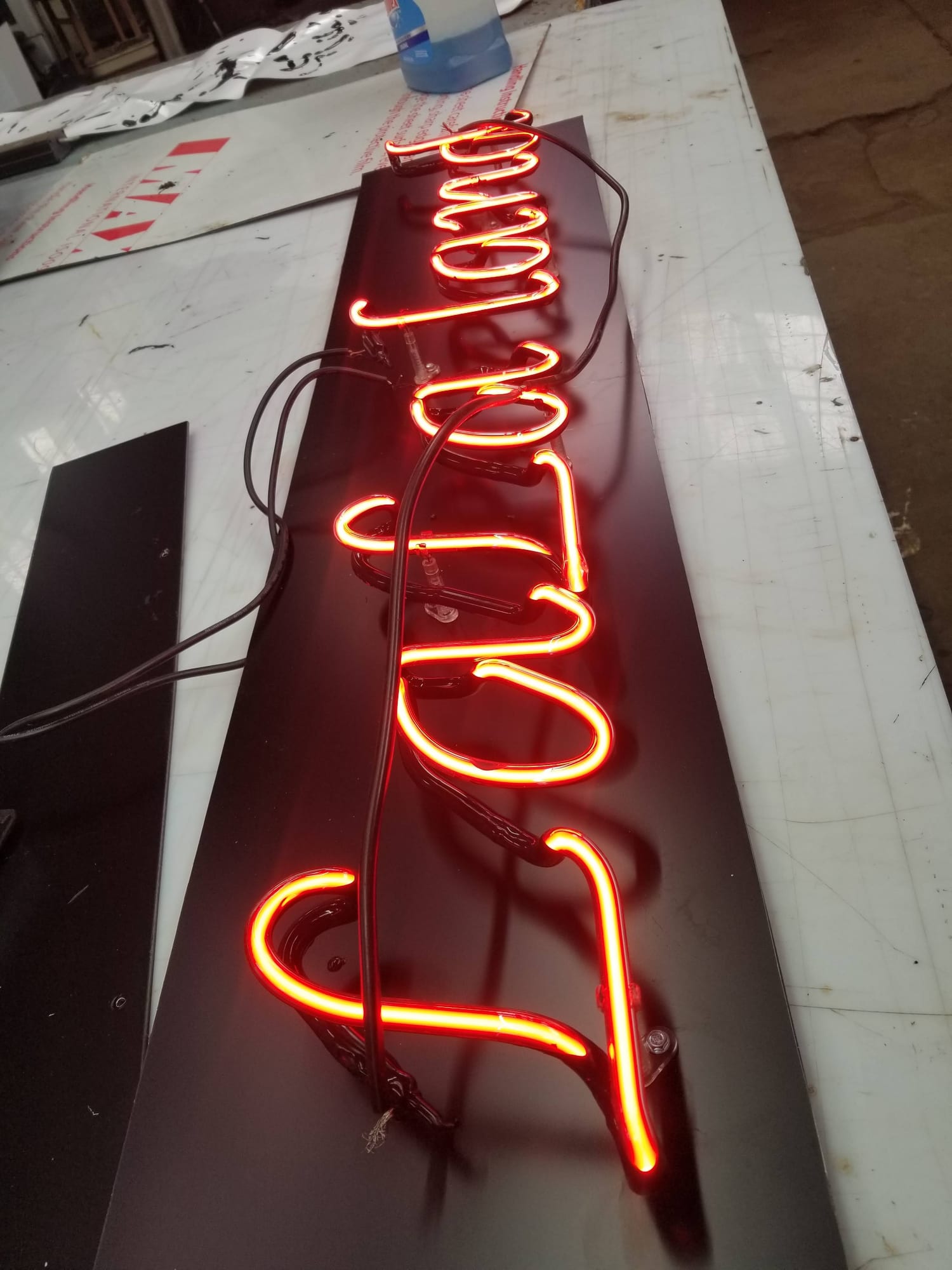 Red neon script mounted on a black sign panel and lit in the shop