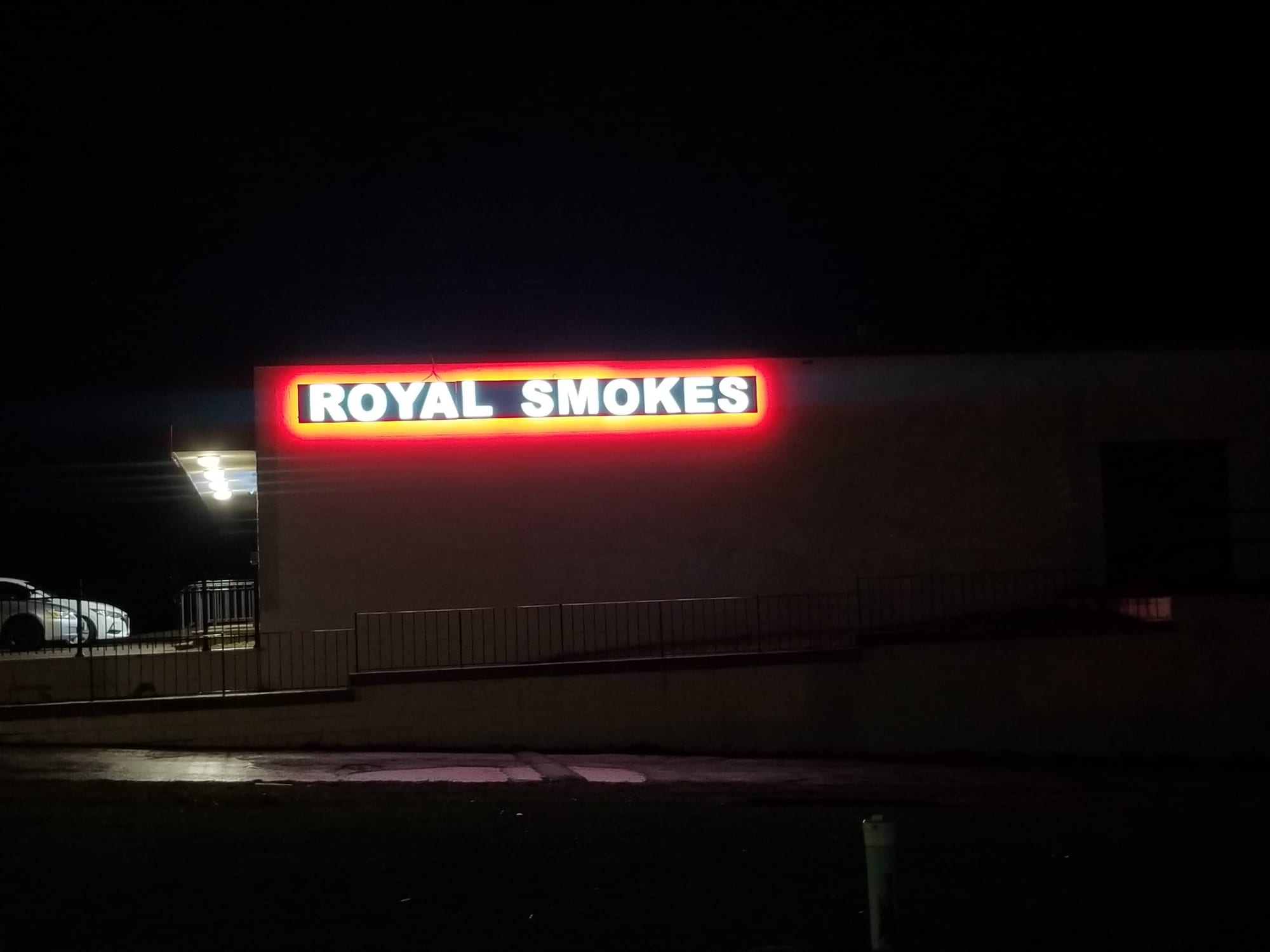 ROYAL SMOKES sign with red halo glow lit on a building wall at night