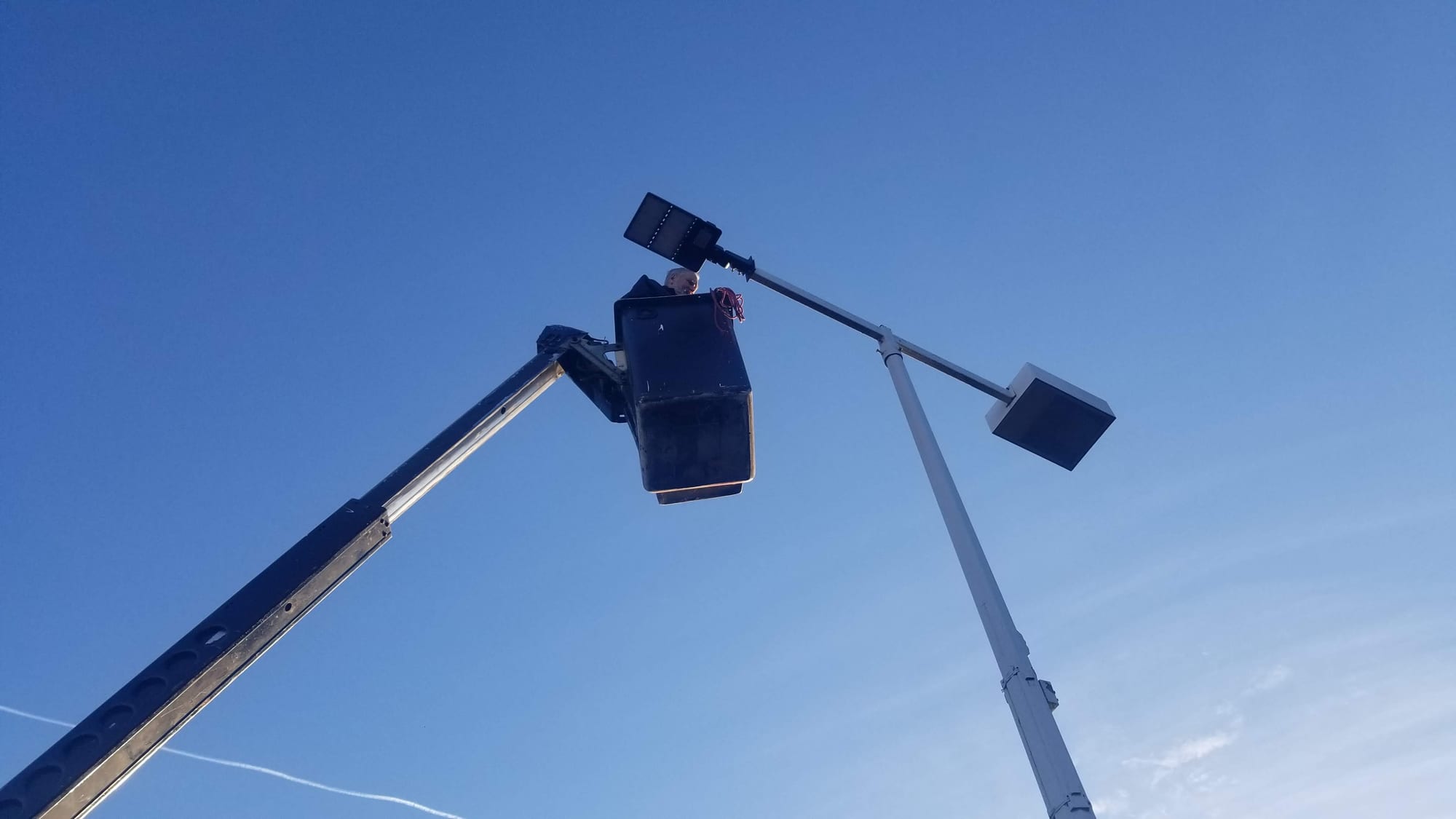 Bucket truck boom raising a worker to a two-head parking lot light pole