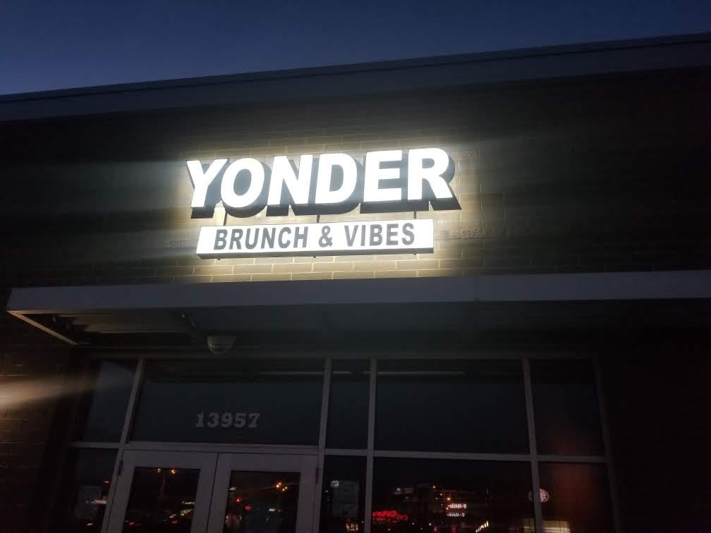 Illuminated YONDER BRUNCH & VIBES letters lit on a brick storefront at dusk
