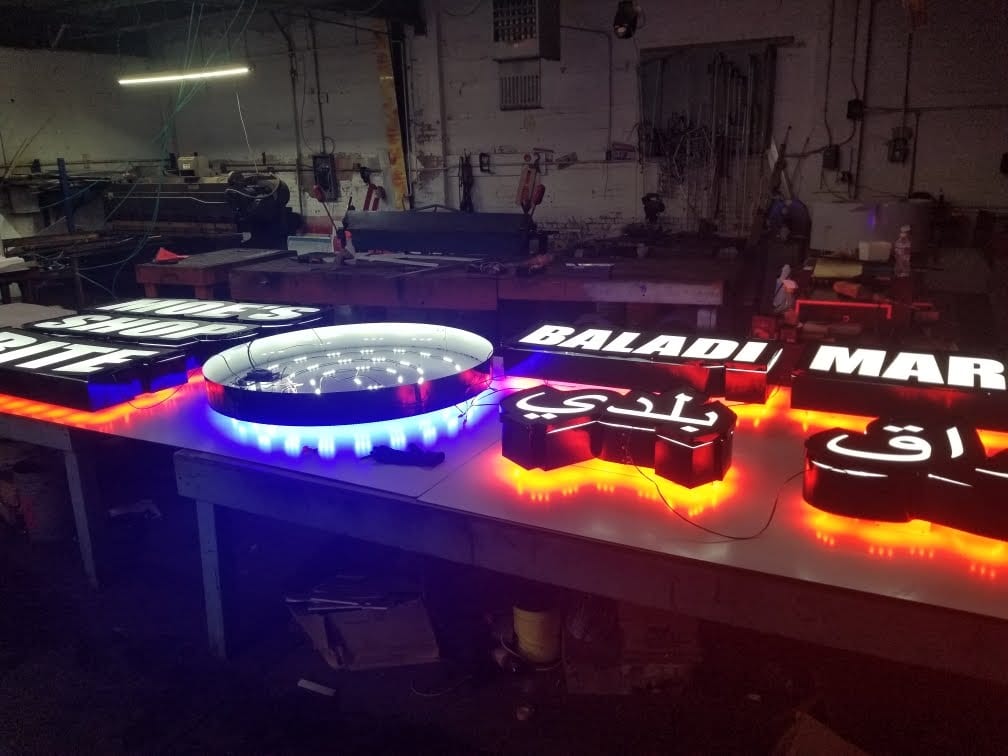 Lit channel letter signs including BALADI on a shop table with red and blue halo glow