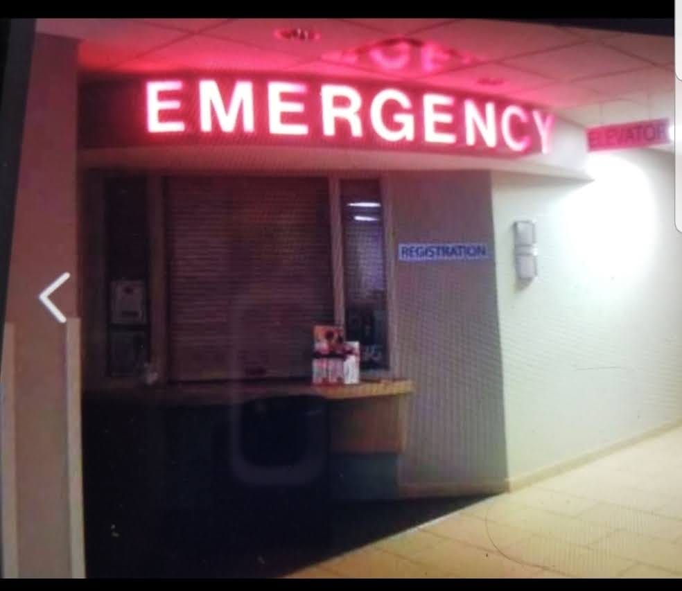 Illuminated EMERGENCY letters glowing red above a hospital registration window