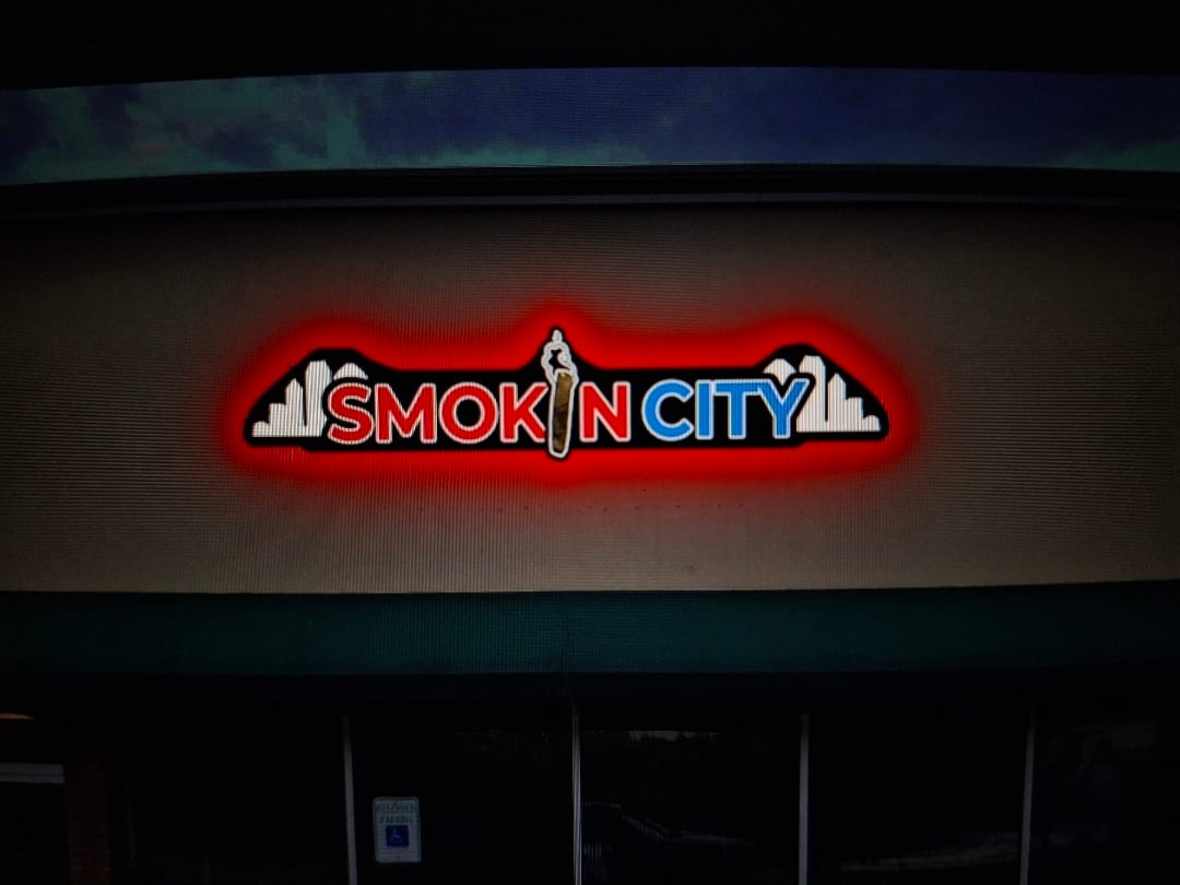 Smokin City halo-lit logo sign glowing red above a storefront at night