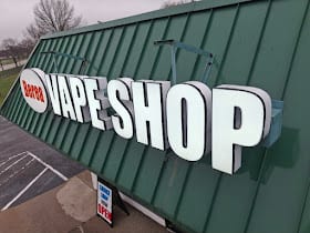 Illuminated VAPE SHOP channel letters mounted on a green metal building fascia