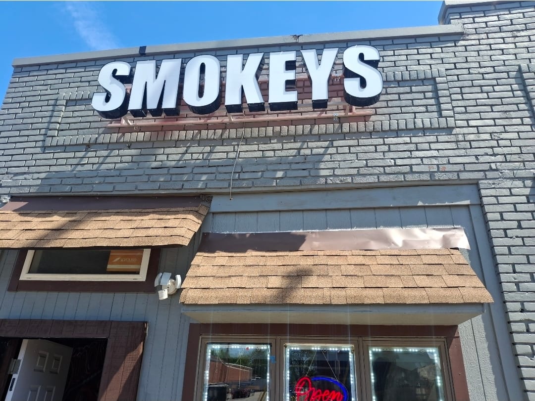 White SMOKEYS channel letters mounted on a grey brick storefront above the entrance