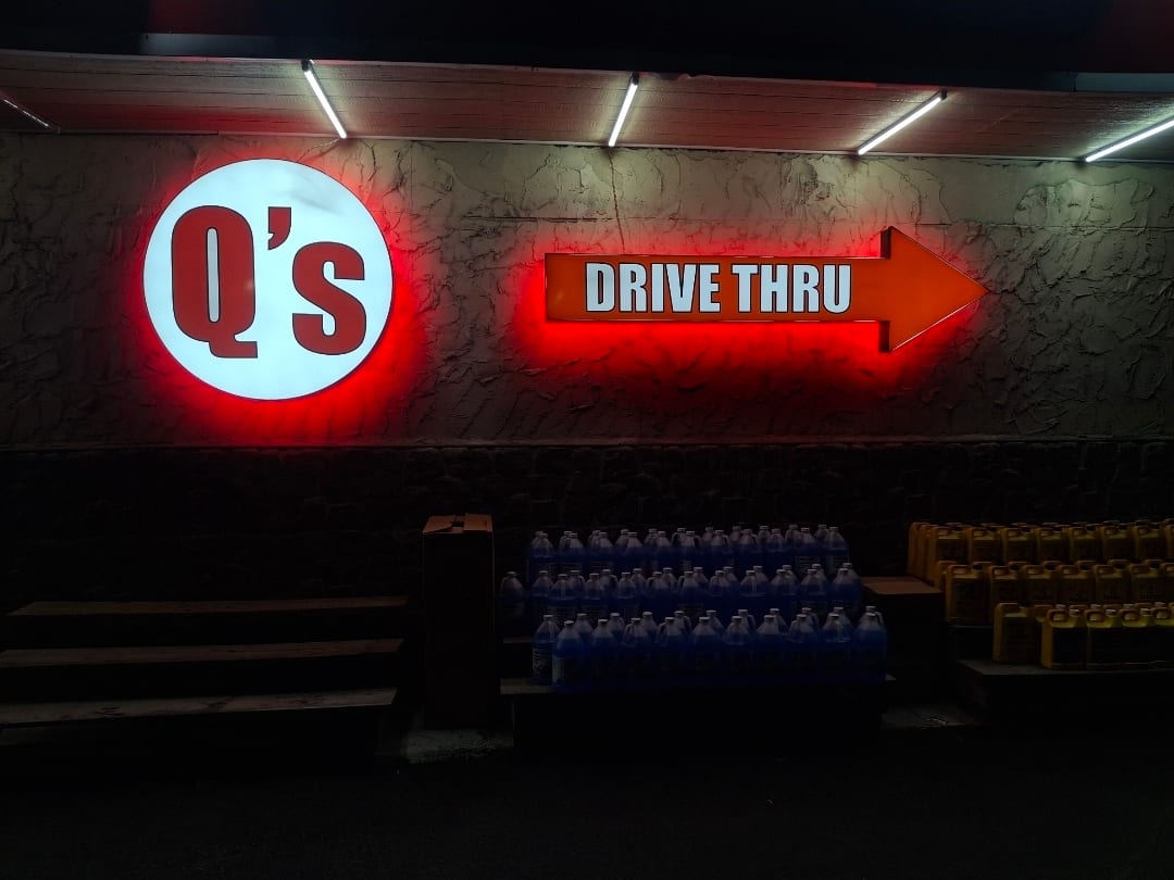 Q's round logo sign and DRIVE THRU arrow cabinet glowing red on a stone wall at night