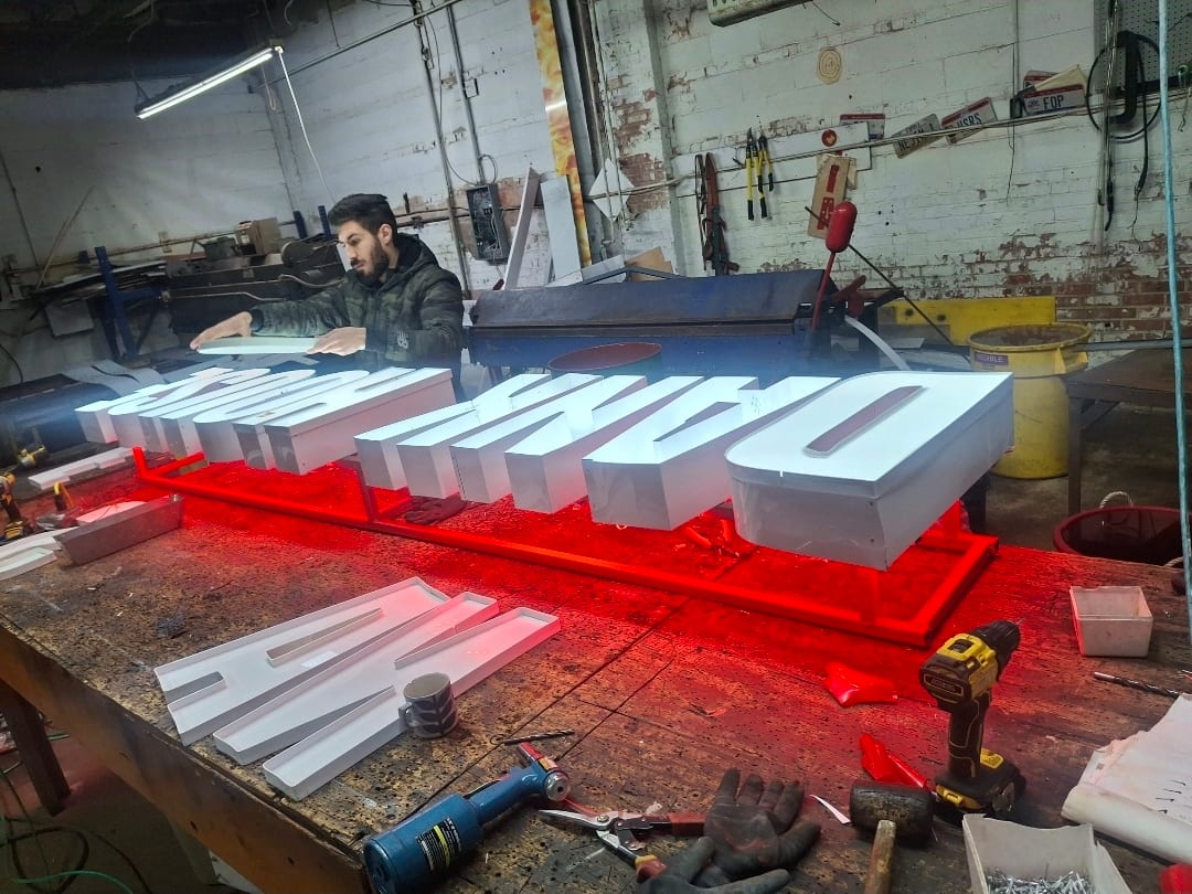Worker assembling white channel letters on a red raceway at a shop workbench