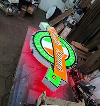 Shaped logo sign with green face and red halo glow resting on the shop floor
