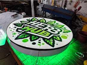 Round HERB HUB lightbox lying on a bench in the shop and lit green