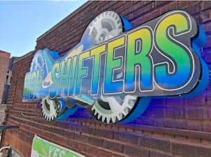 Shaped SHIFTERS logo cabinet with gear artwork mounted on a brick wall