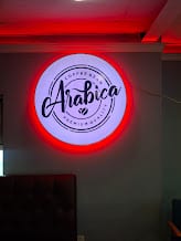 Round Arabica logo sign with red halo glow mounted on an interior wall