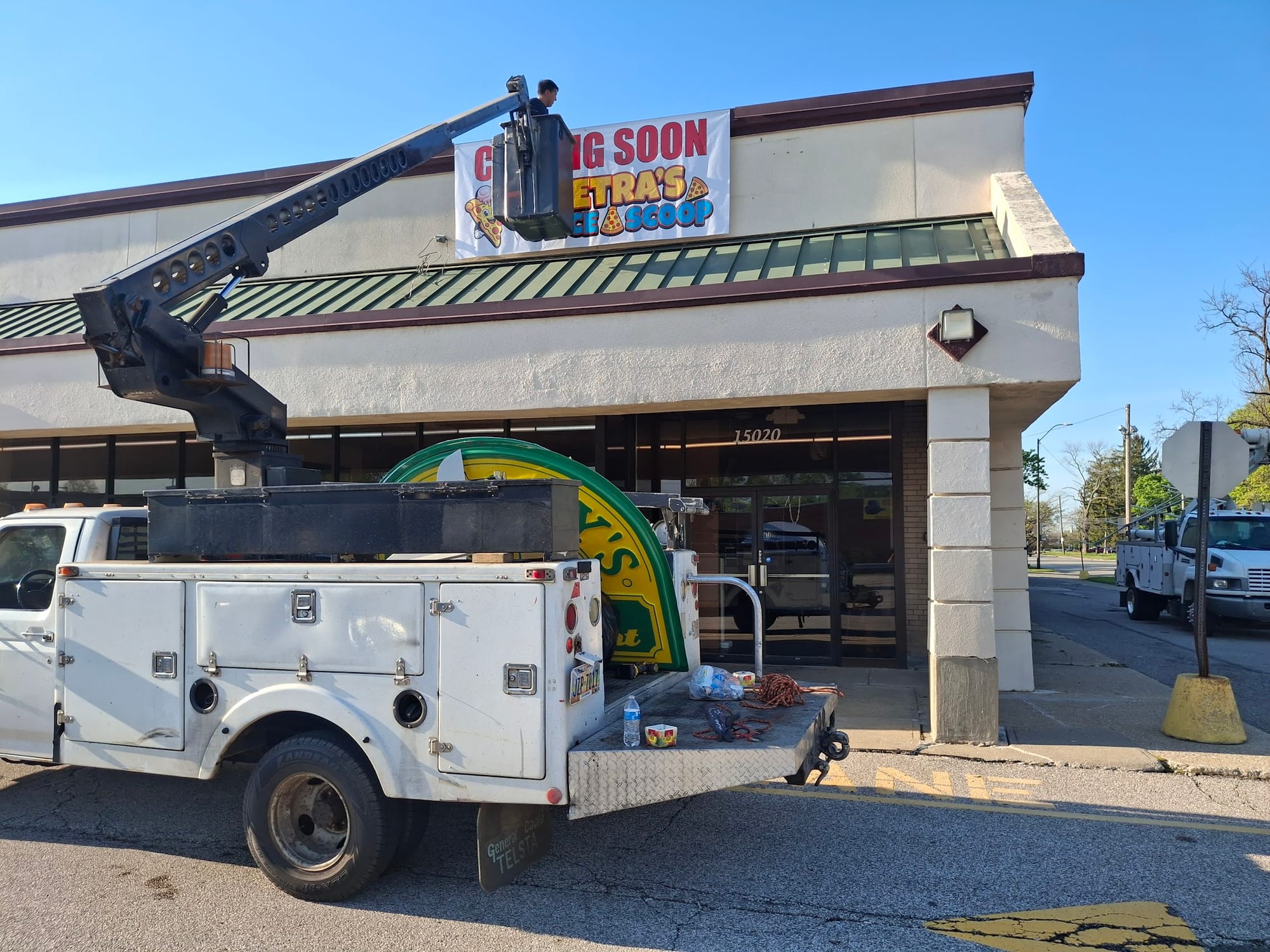 Crew member in a bucket lift hanging a COMING SOON banner on a storefront fascia
