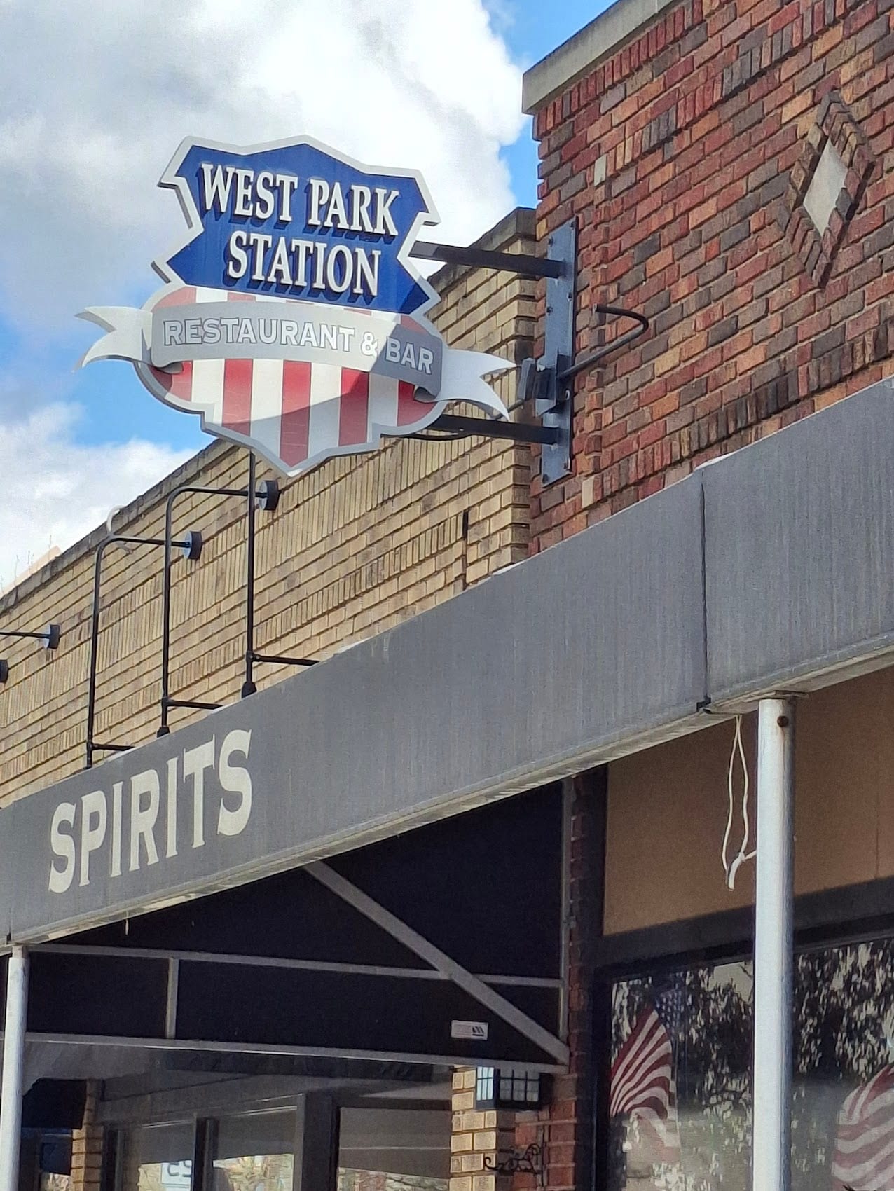 West Park Station Restaurant & Bar shaped blade sign mounted on a bracket off a brick wall
