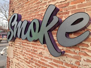 Dimensional script letters reading smoke mounted on a red brick wall