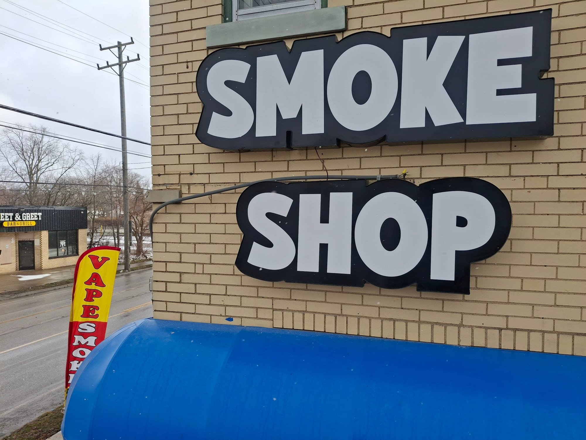 Large SMOKE SHOP letters on black backer panels mounted to a tan brick wall