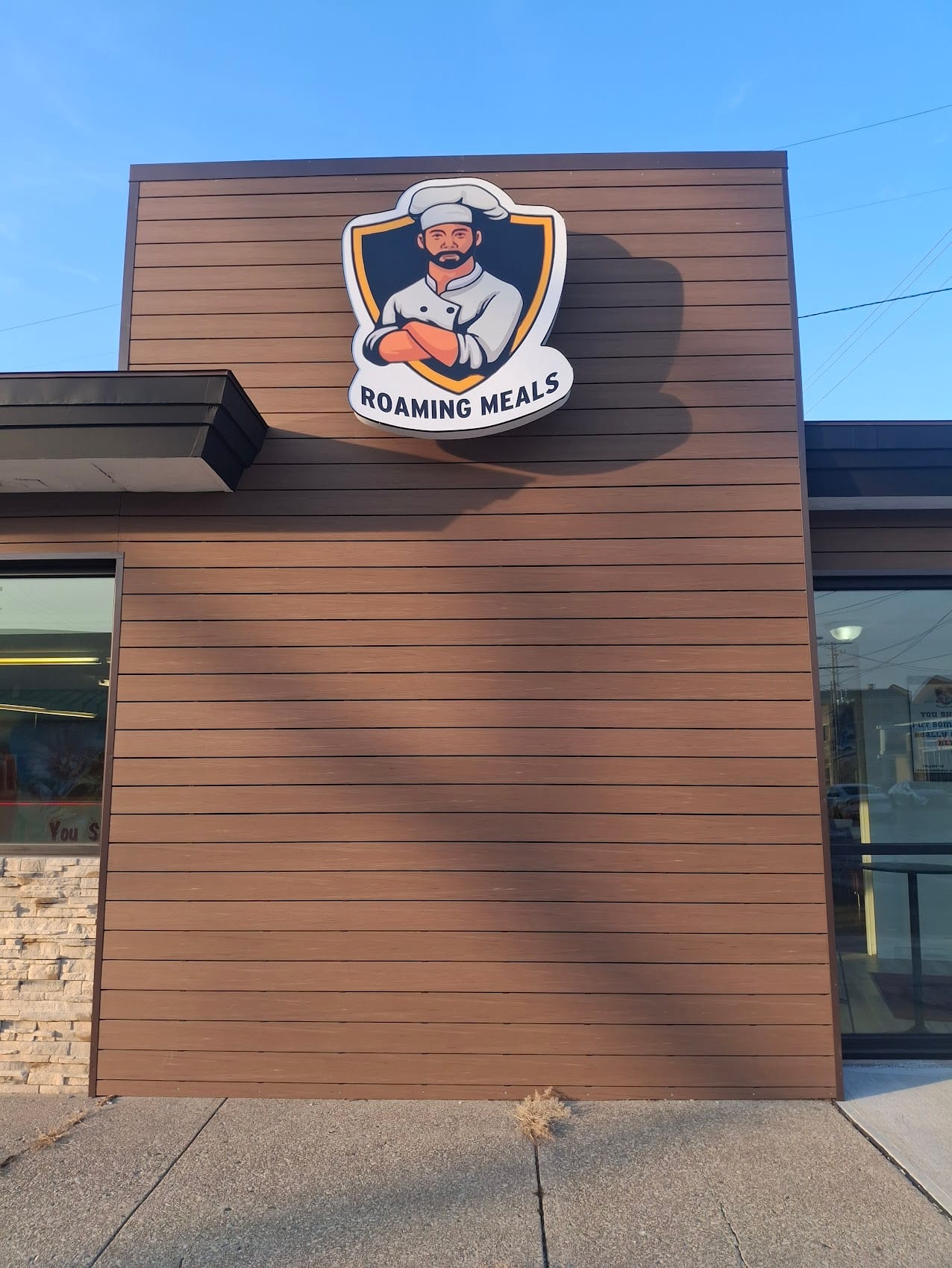 Roaming Meals logo cabinet sign mounted on a wood-clad storefront wall