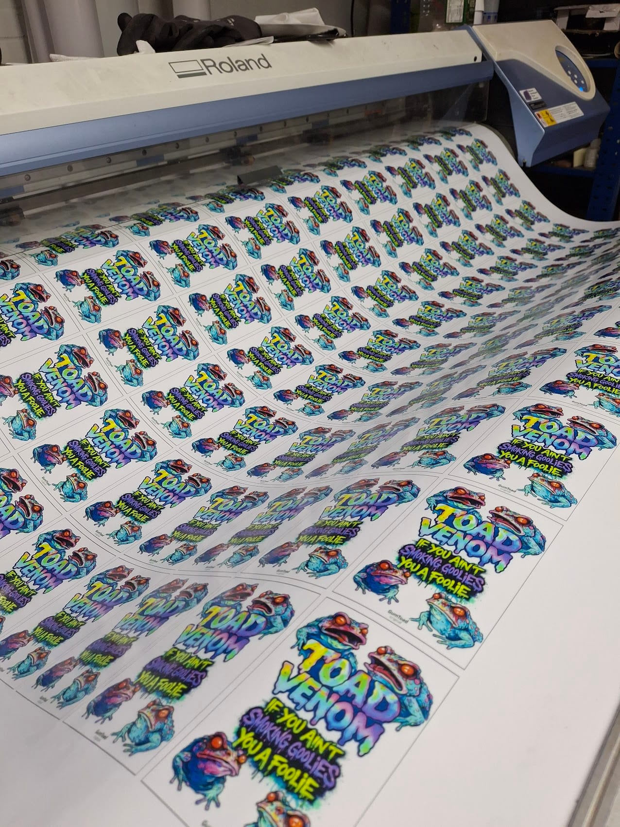 Roland wide-format printer running a full sheet of Toad Venom vinyl stickers