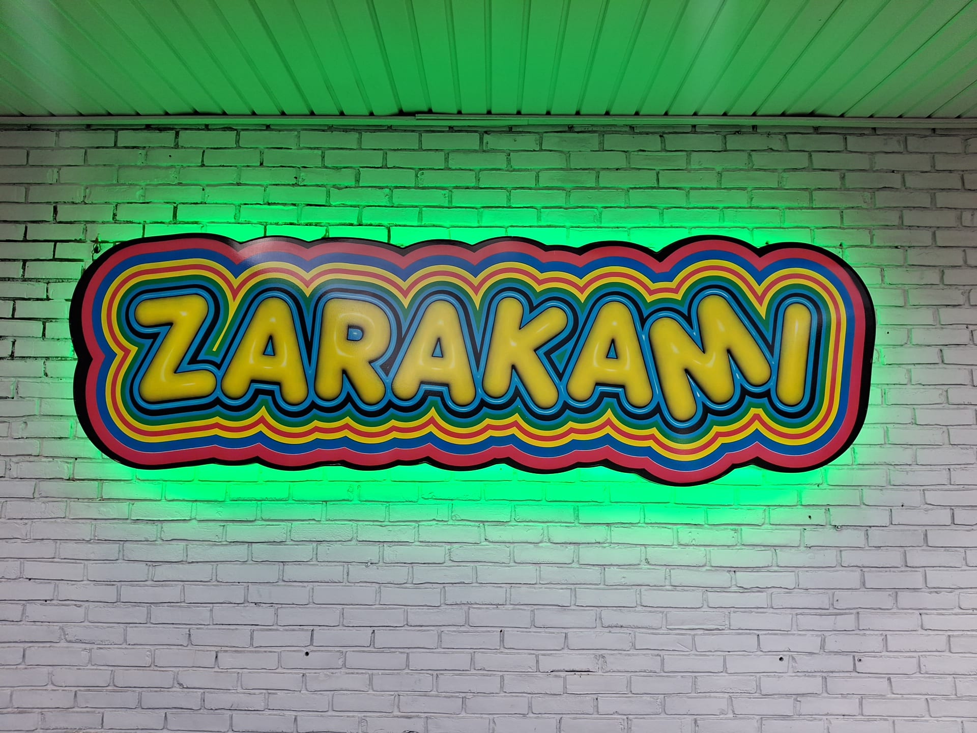 Halo-lit ZARAKAMI shaped cabinet sign glowing green on a white brick wall